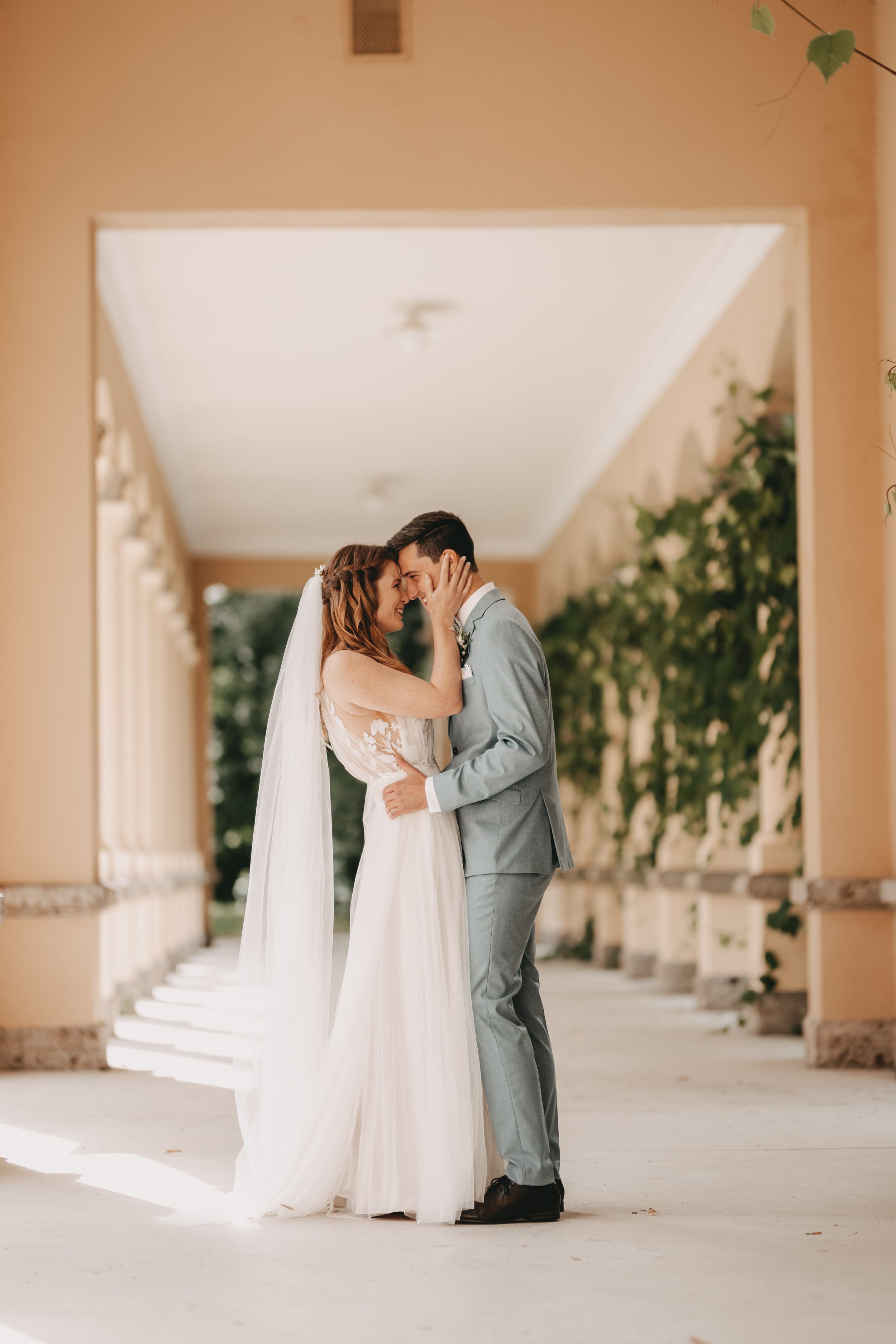Romantic wedding couple embracing in an elegant covered walkway.