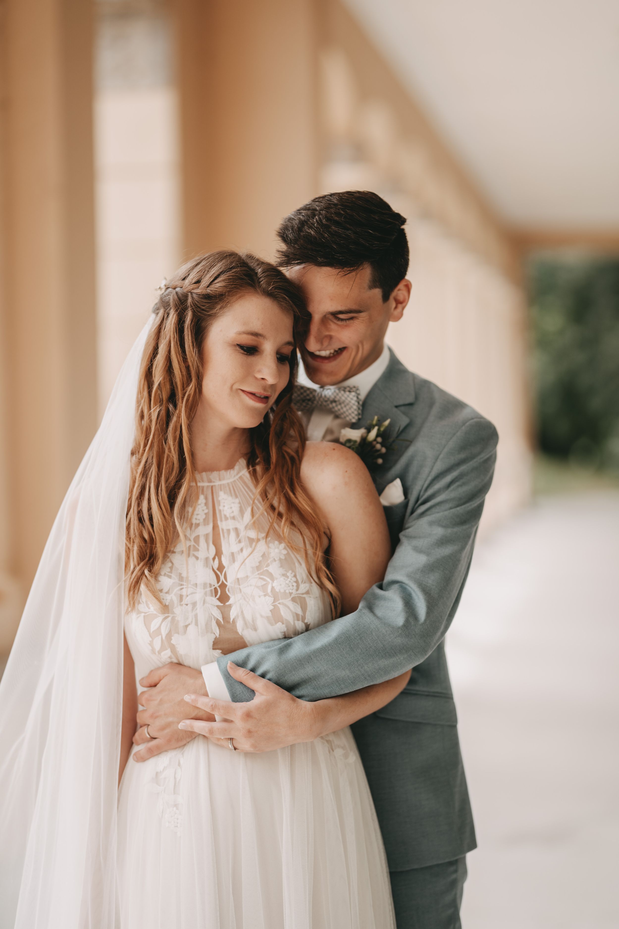 Intimate wedding couple embrace in sunlit colonnade with romantic lighting.