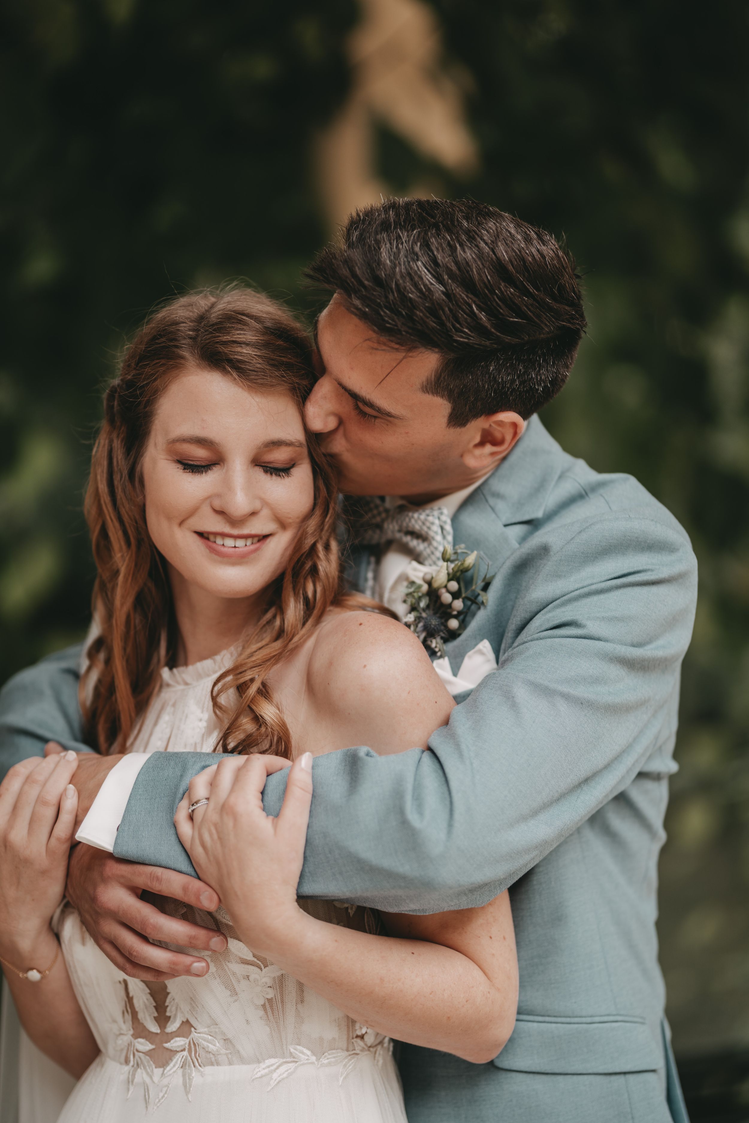 Romantic wedding couple embraces outdoors in an intimate moment with soft natural lighting.