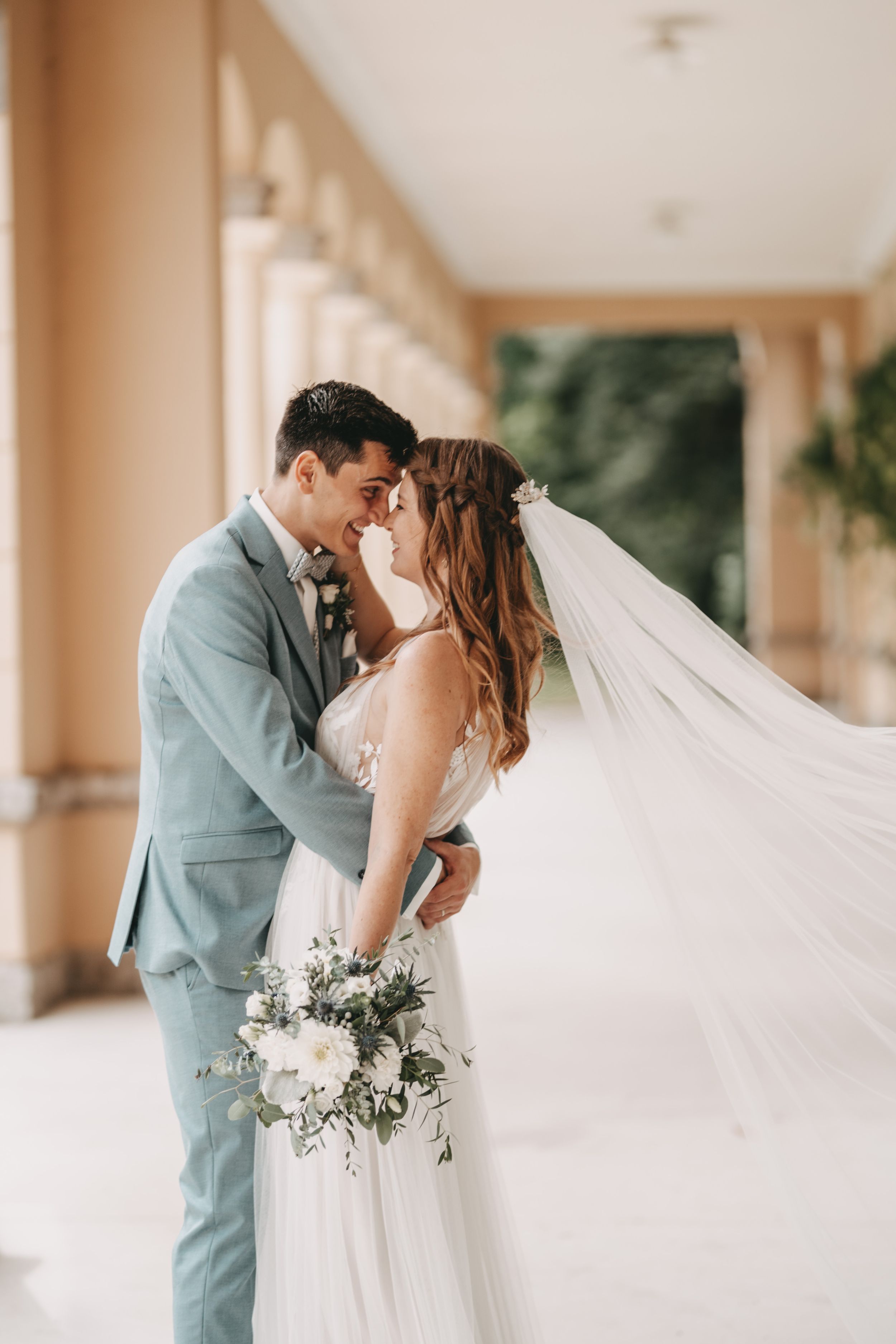 Bride and groom share romantic moments in an elegant colonnade with flowing veil.