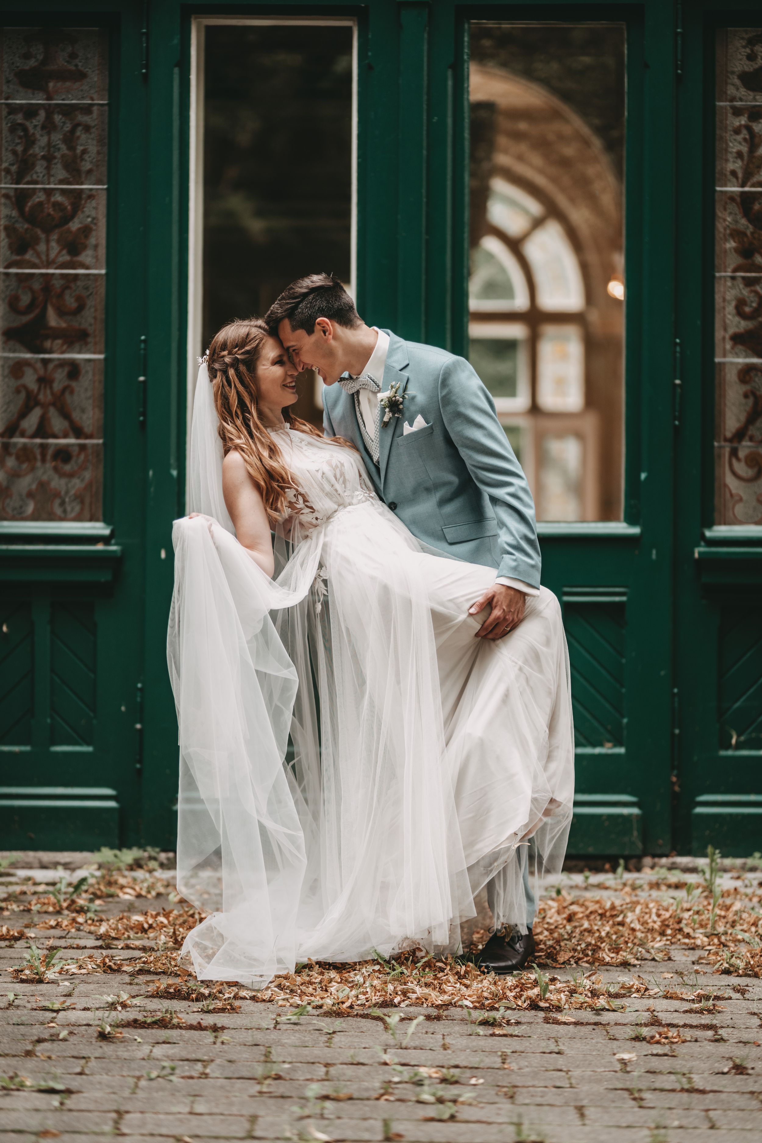 Romantic wedding photo session by vintage green doors with autumn leaves.