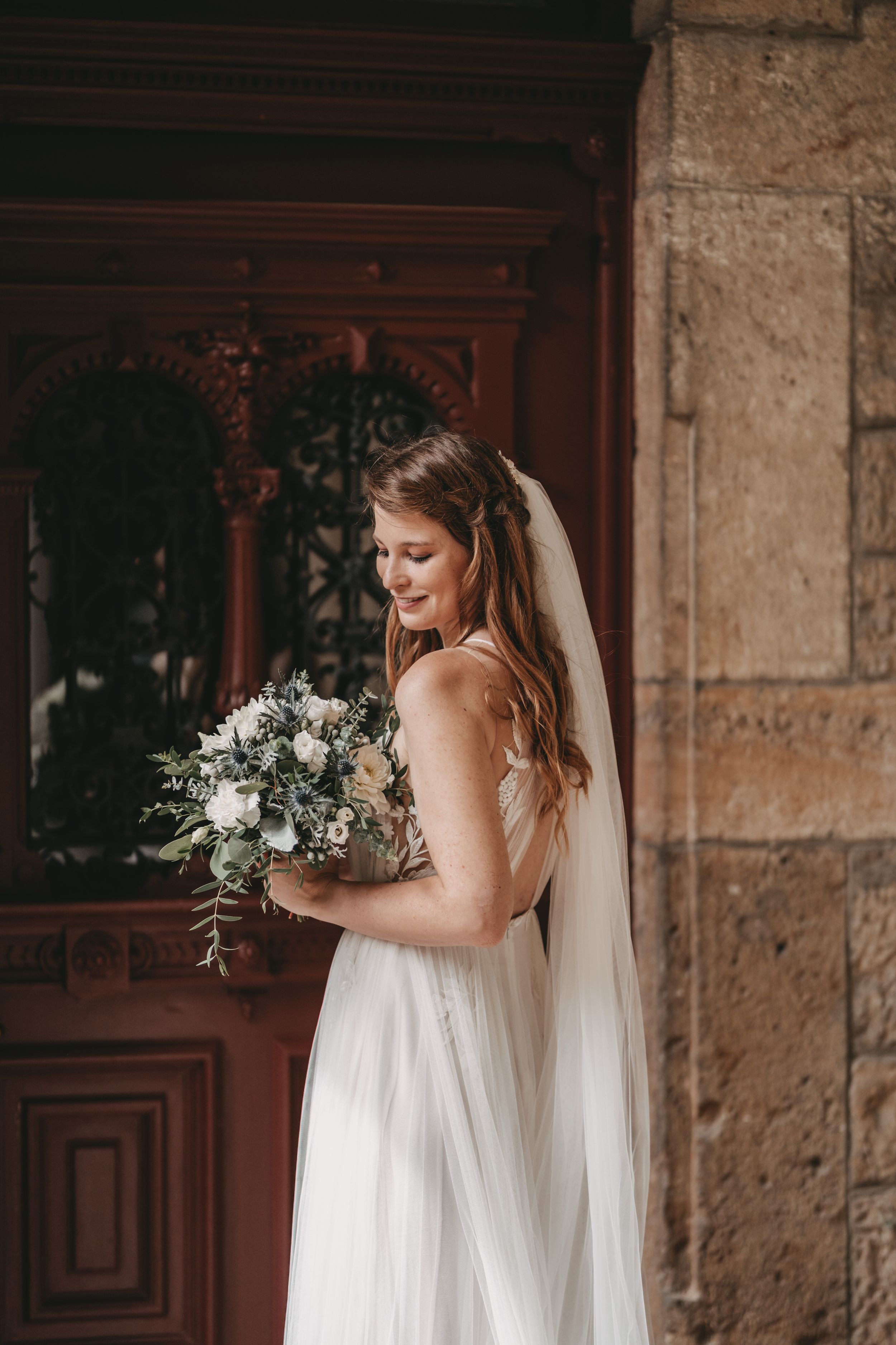 Bride in white dress poses gracefully against stone architecture with wooden doors.