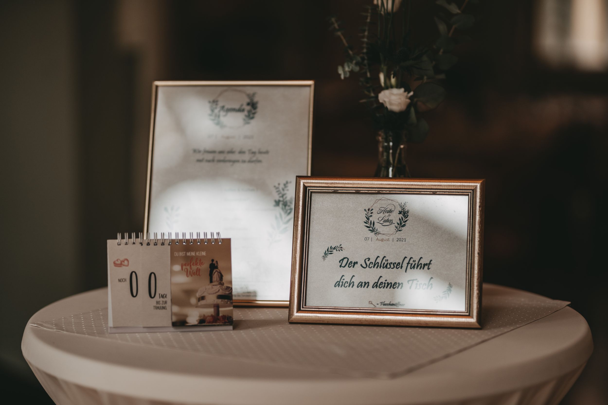 Framed wedding signs and calendar displayed on a round table with romantic decor.