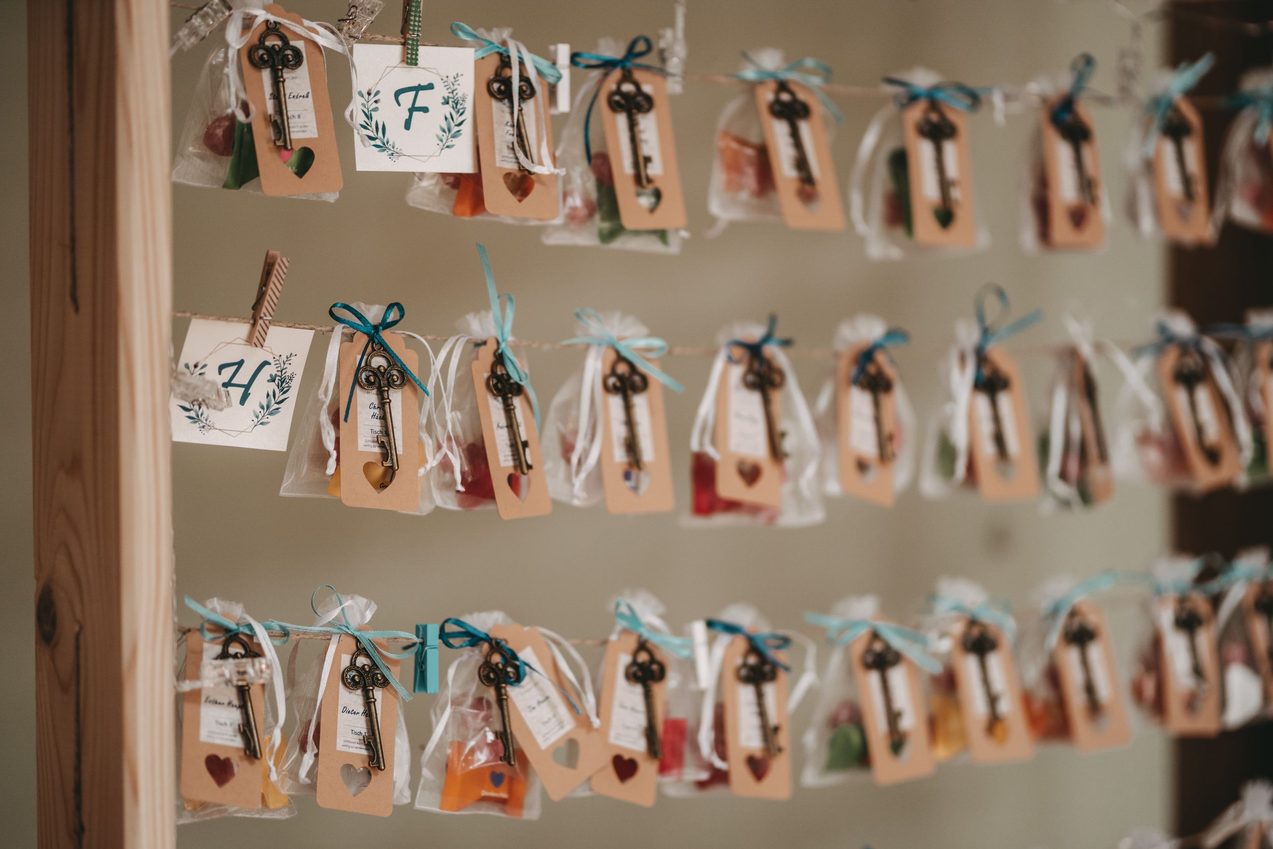 Wedding favor bags with numbers hanging on strings against a neutral wall.