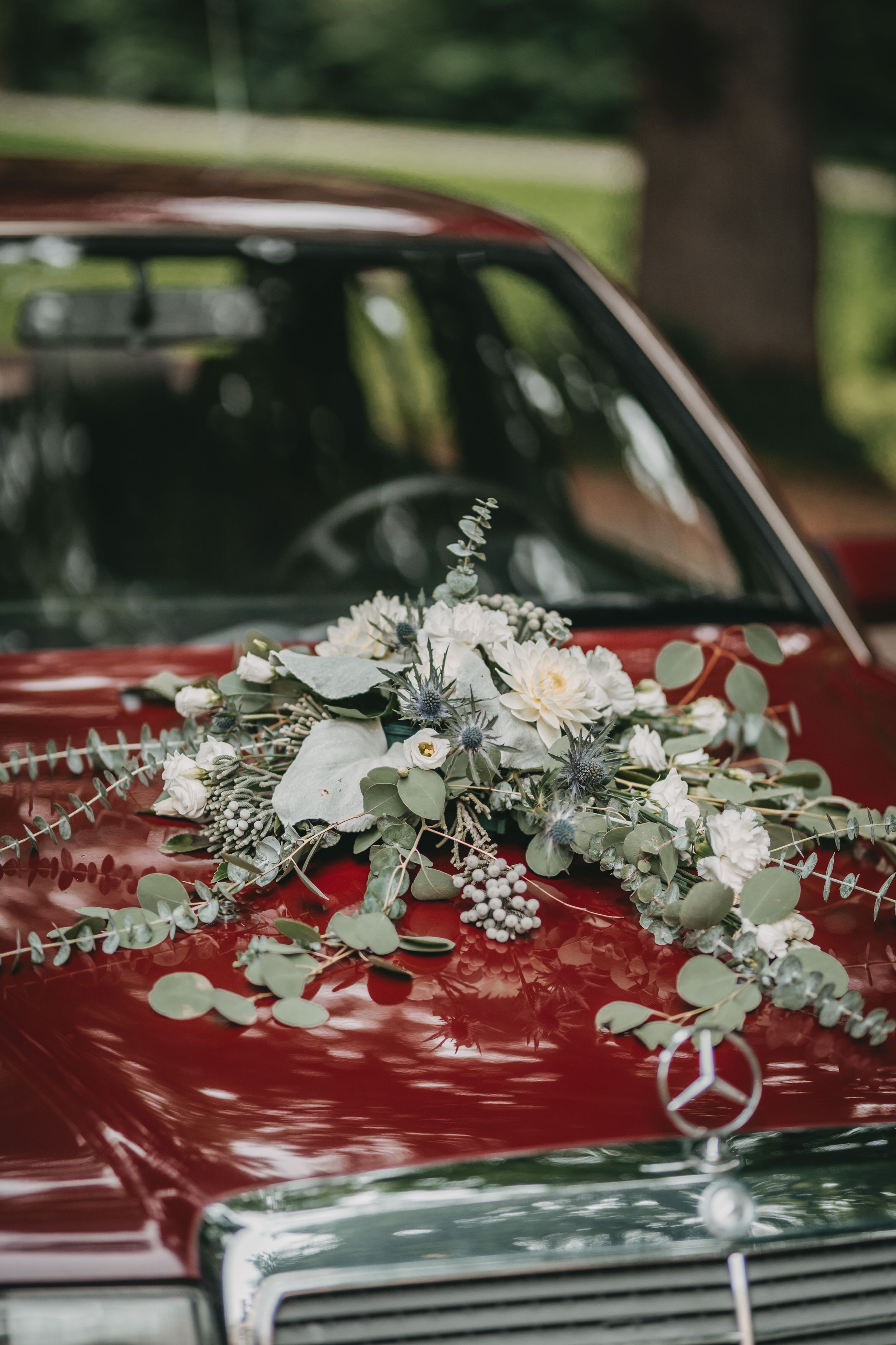 Elegant floral arrangement with white blooms decorating a red Mercedes-Benz hood.
