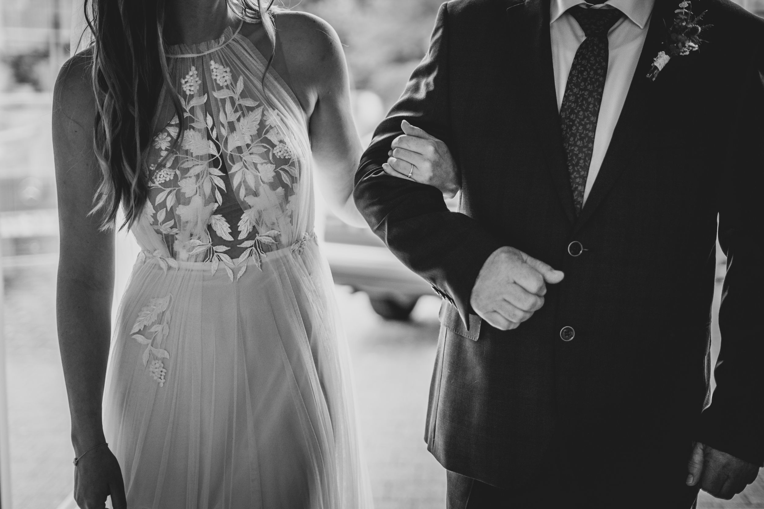 Close-up of a bride's lace dress detail and groom's suit in black and white.
