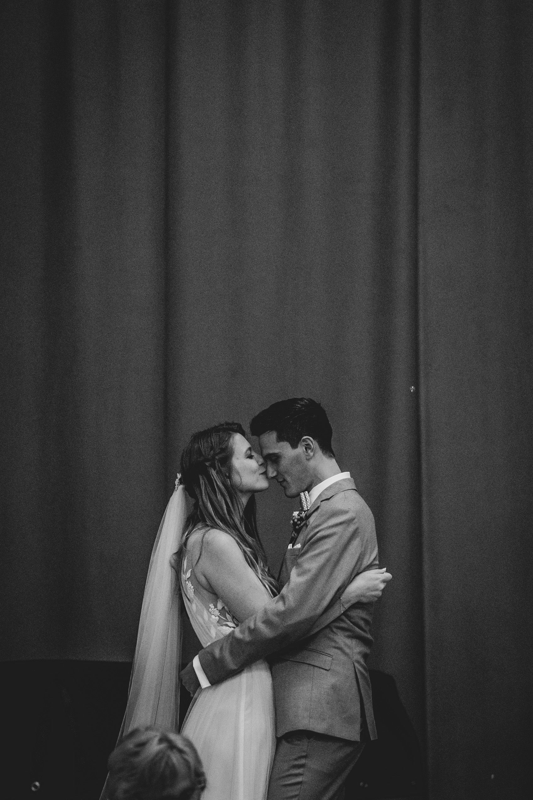 An intimate black and white portrait of a couple sharing their first kiss as newlyweds.