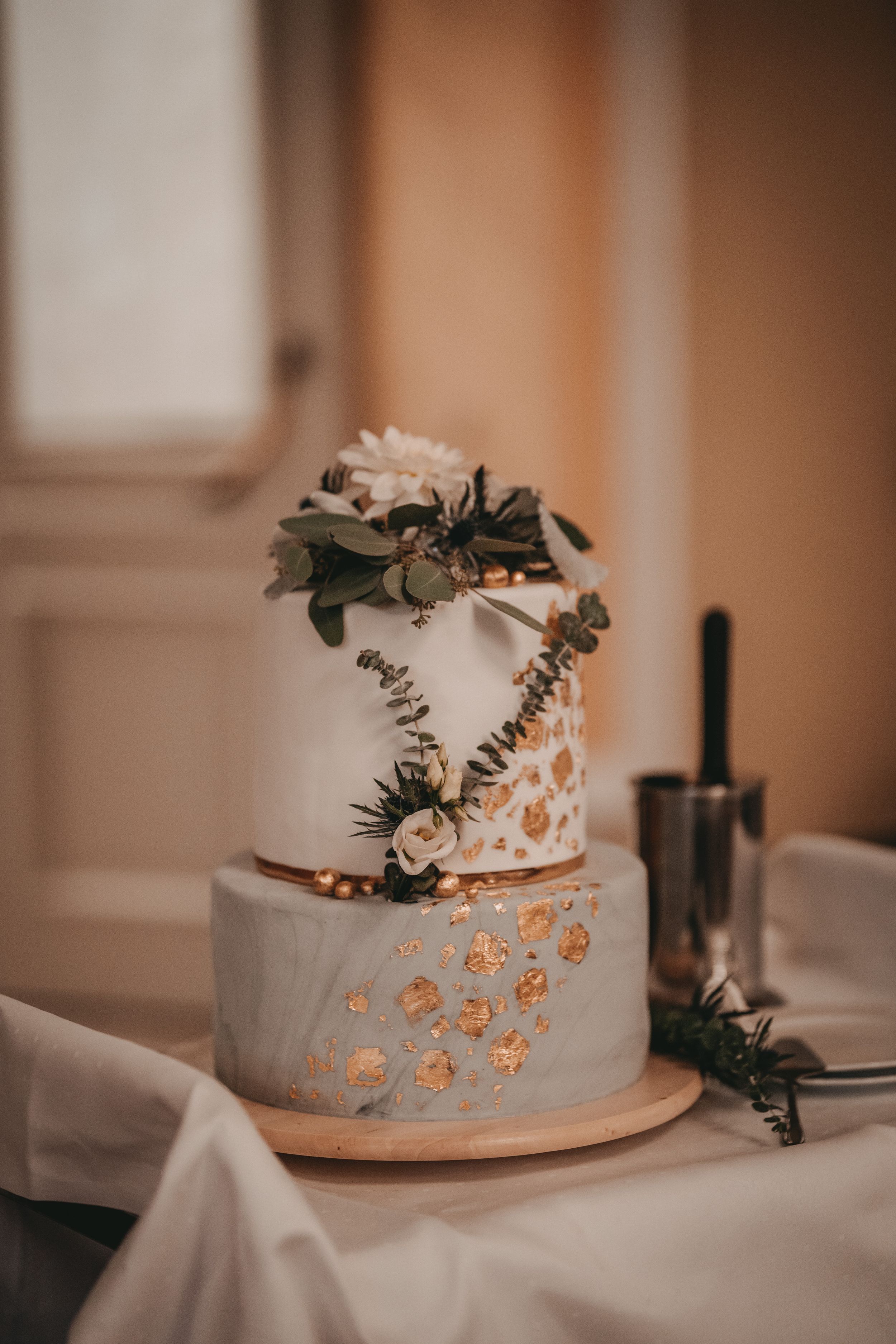 Elegant white wedding cake decorated with delicate floral details and metallic accents on a wooden cake stand.