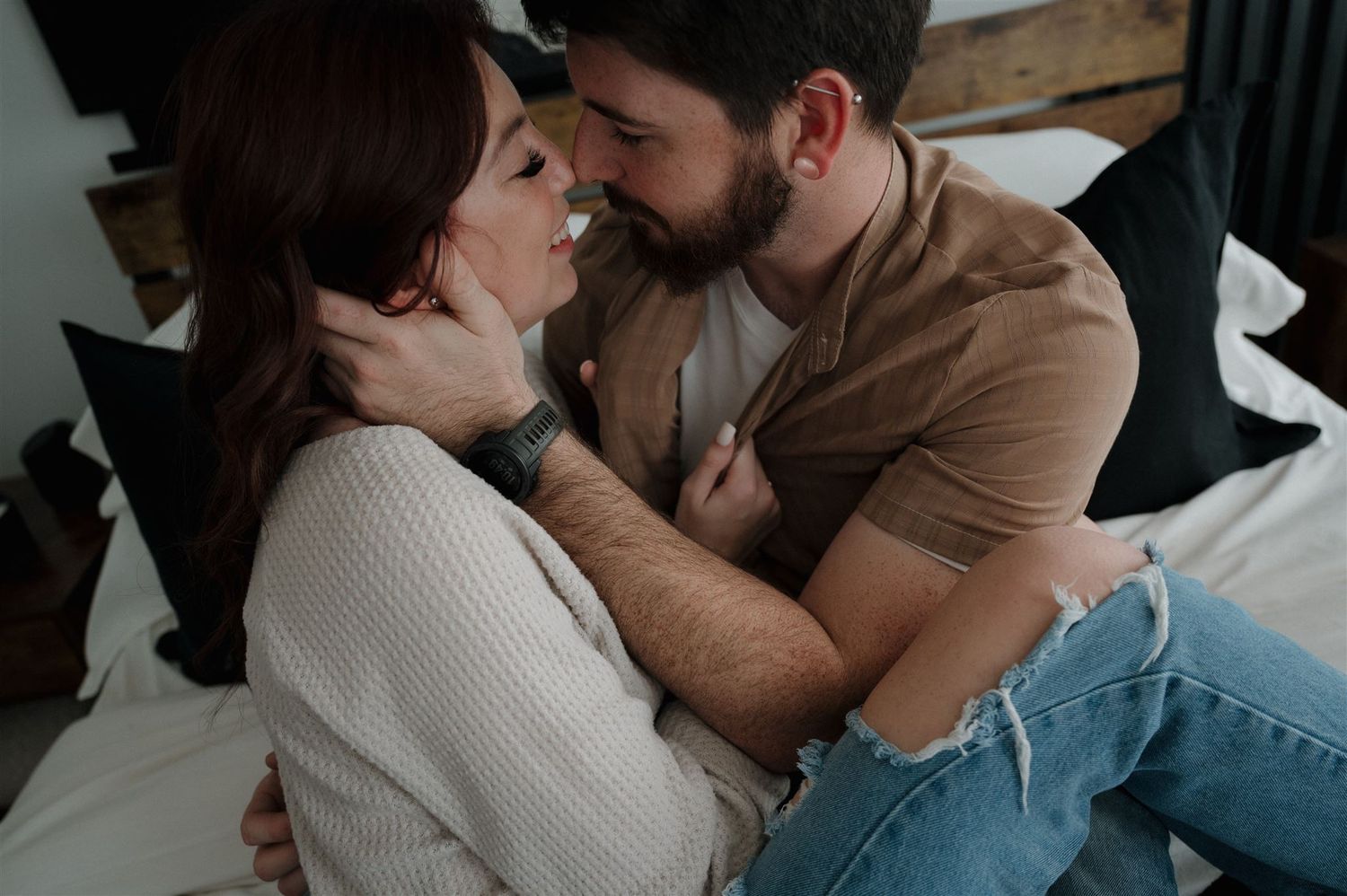 Intimate couple sharing a tender moment while sitting on white bed linens.