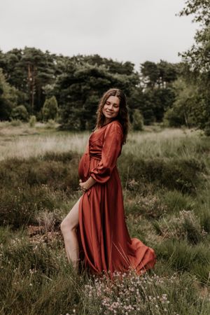 Zwangere vrouw houdt haar buik vast terwijl ze naar het gras kijkt