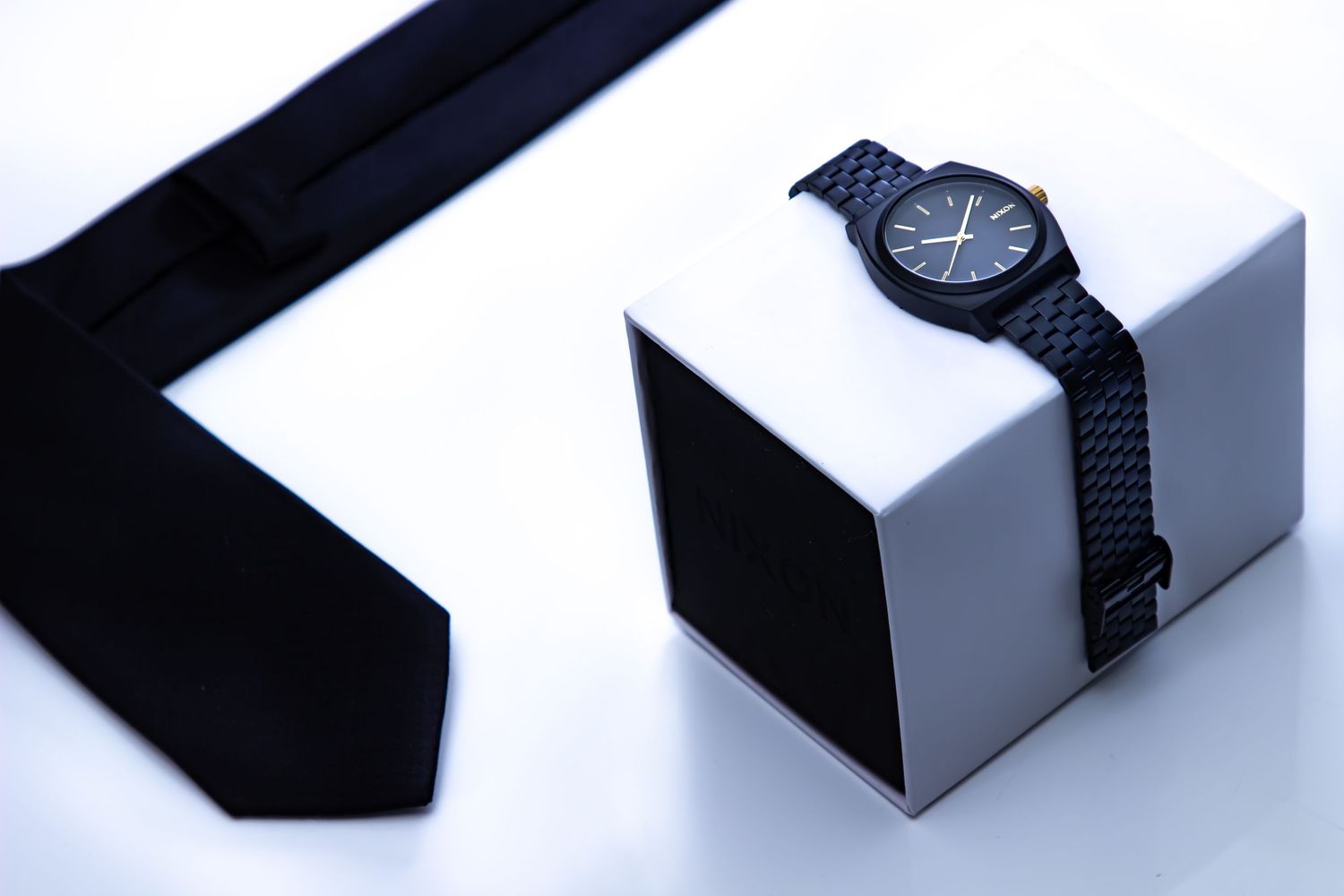 Sleek black watch and tie arranged on white geometric blocks in studio lighting.