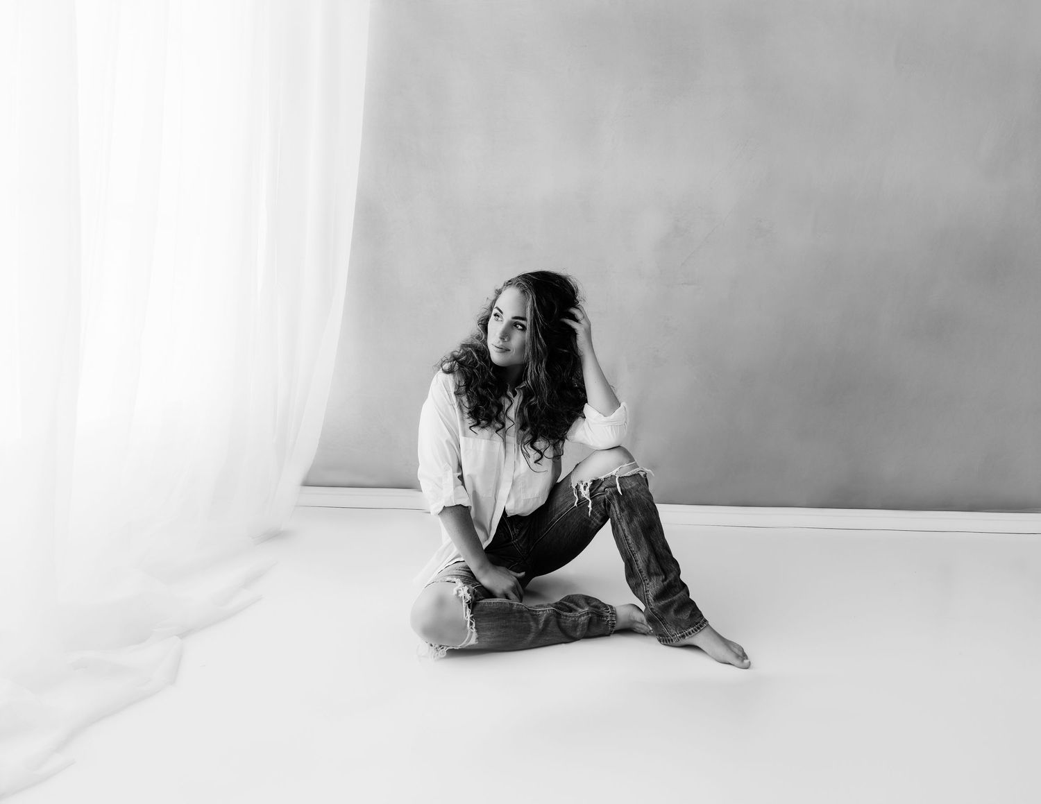 Black and white portrait of woman sitting on floor in casual jeans and white shirt.