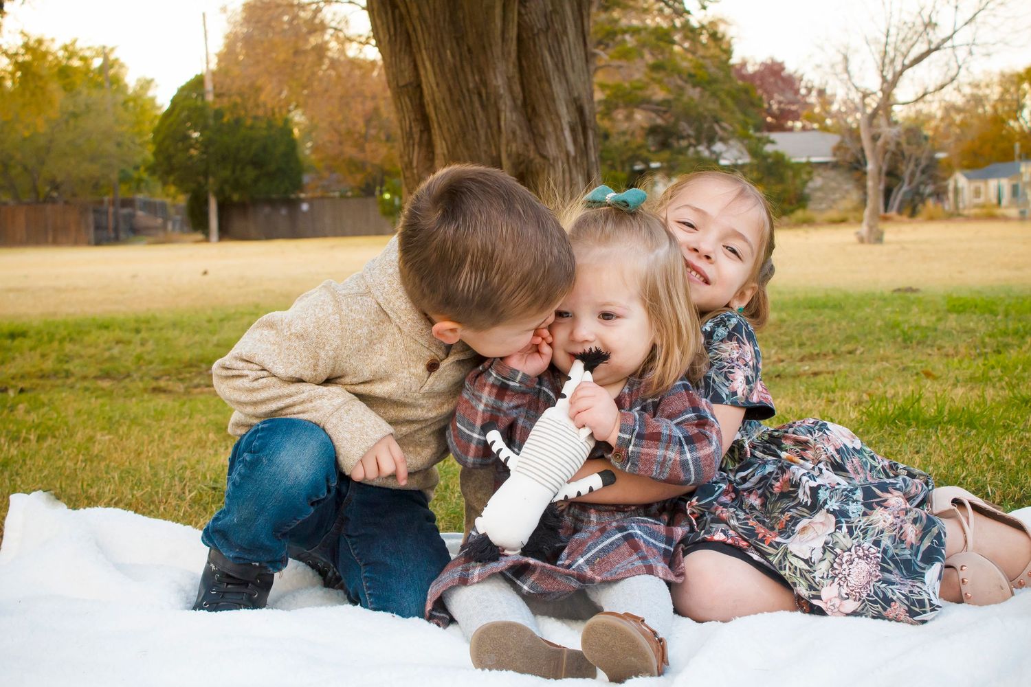 Young children playing and laughing together on a blanket outdoors during autumn.