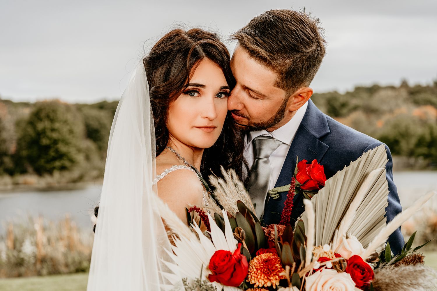 Romantic outdoor portrait with red floral bouquet against natural desert landscape.