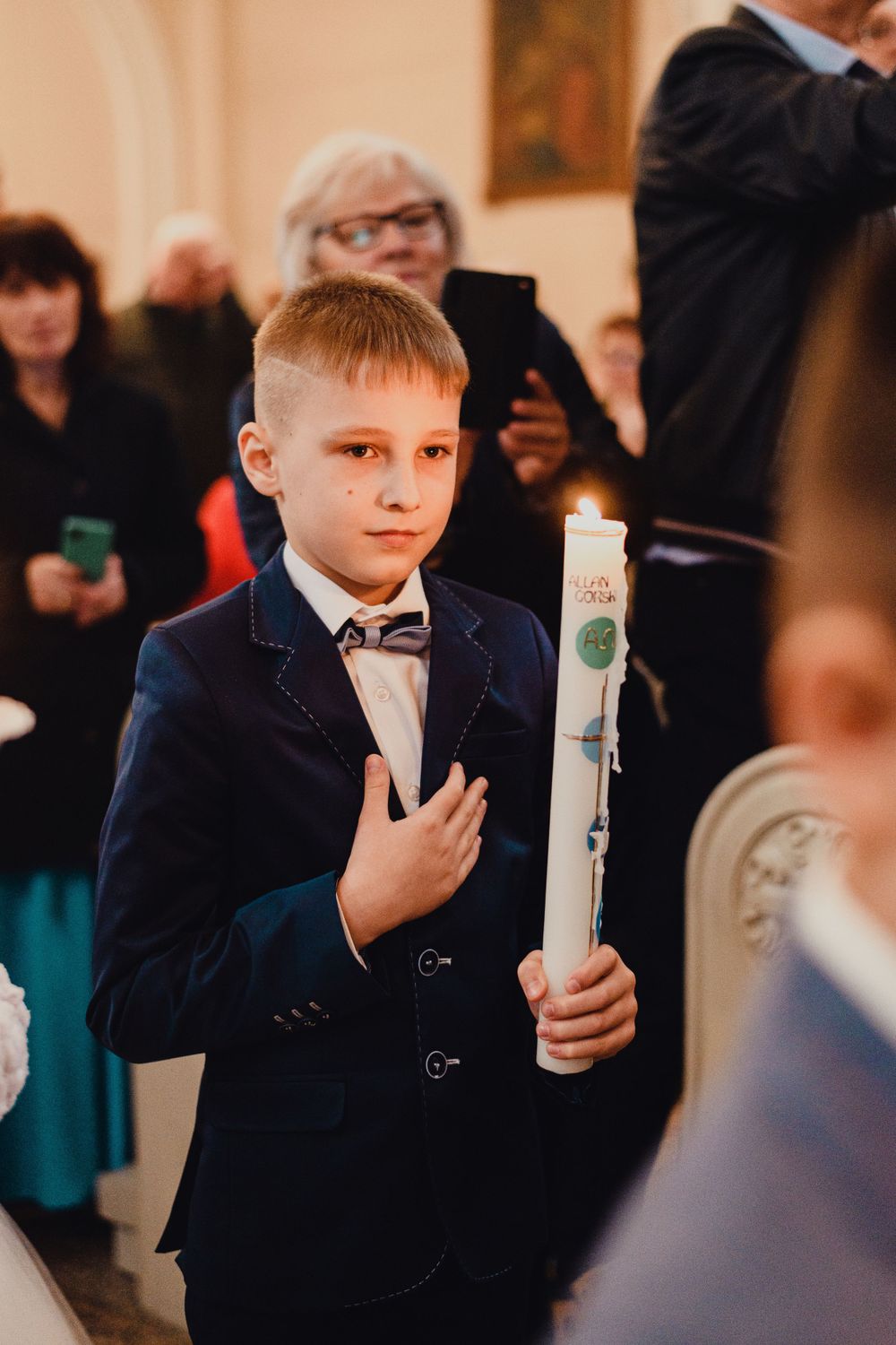 Young participant holding ceremonial candle during religious service in church setting.