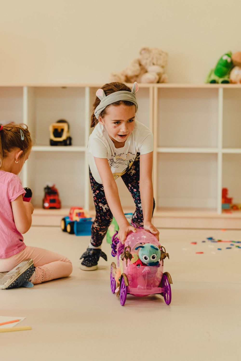 Children playing with toys on floor in playroom with white shelving.