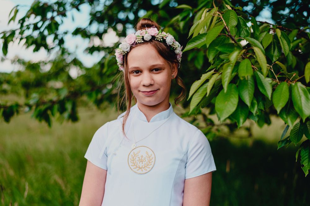 Child wearing floral crown standing in front of green foliage outdoors.