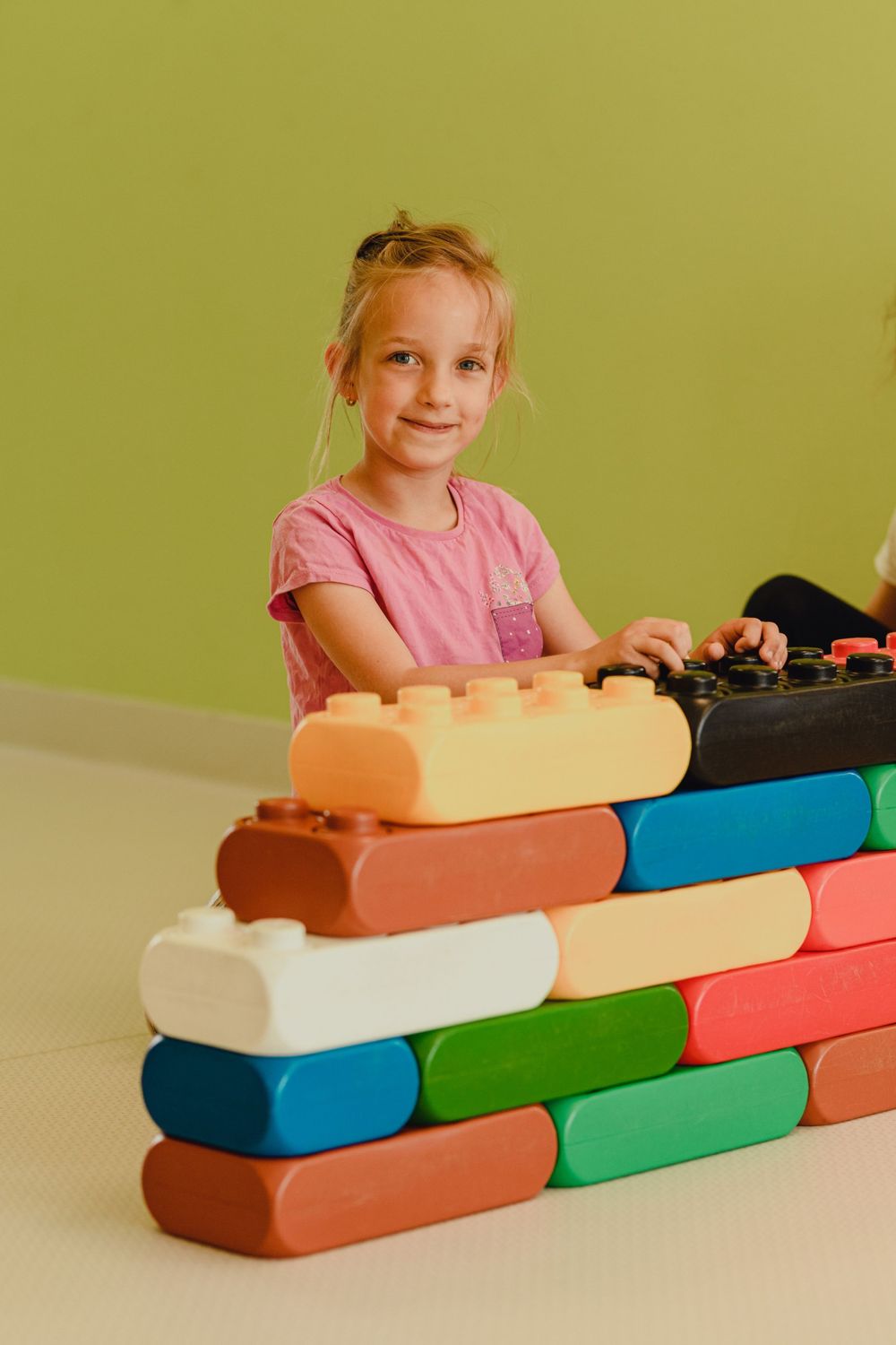 Child playing with colorful building blocks on table against green background.