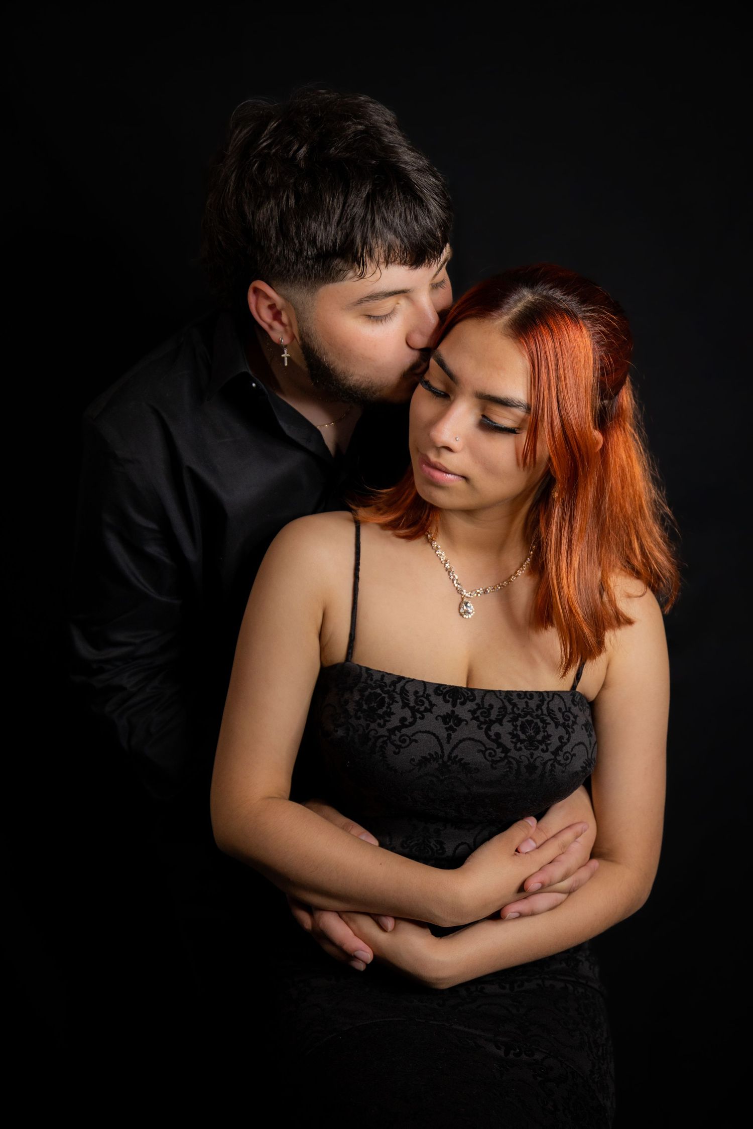 Intimate couple portrait against dark background with dramatic lighting.