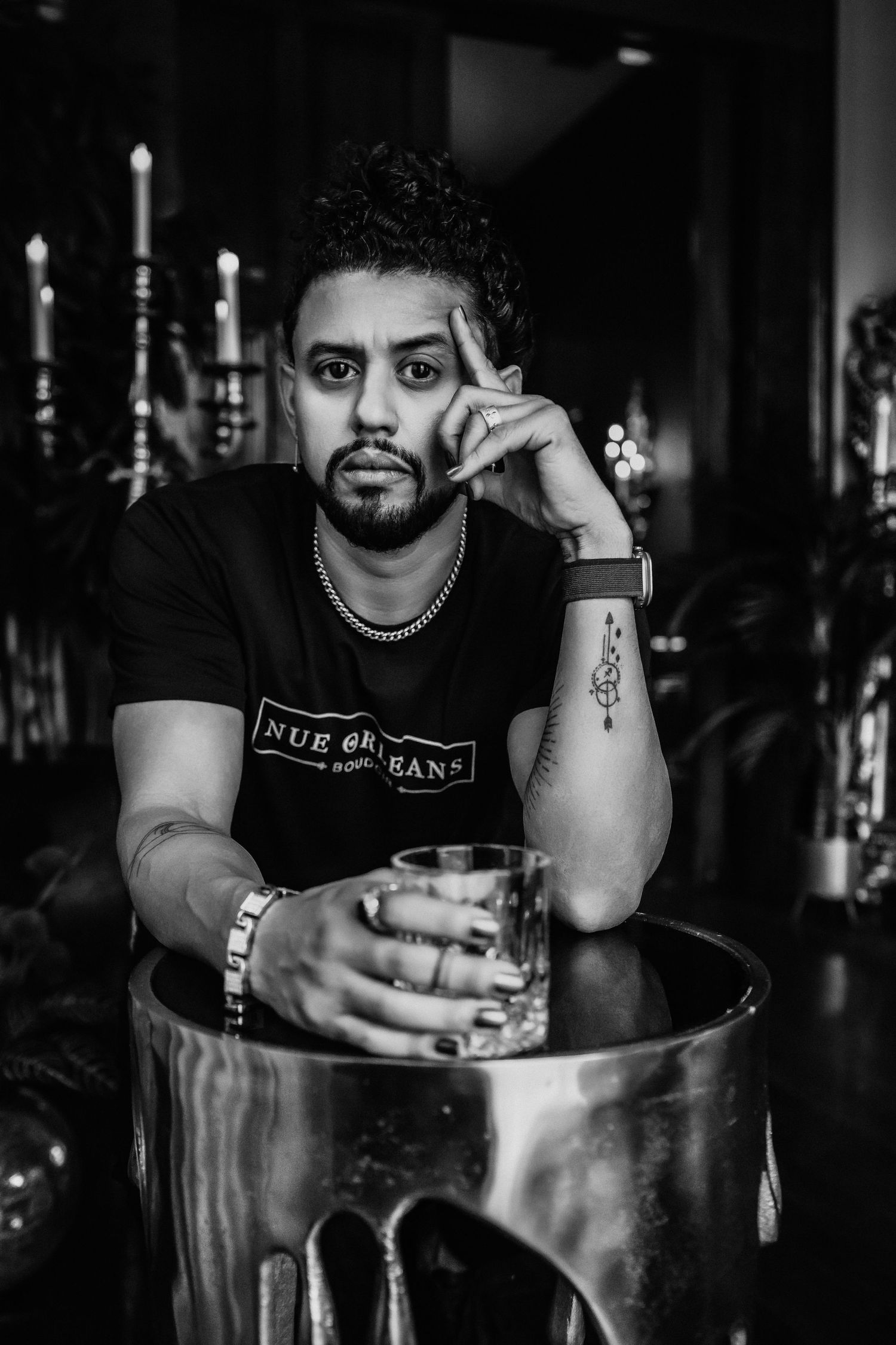 Black and white portrait of someone in a t-shirt holding a drink at a bar.