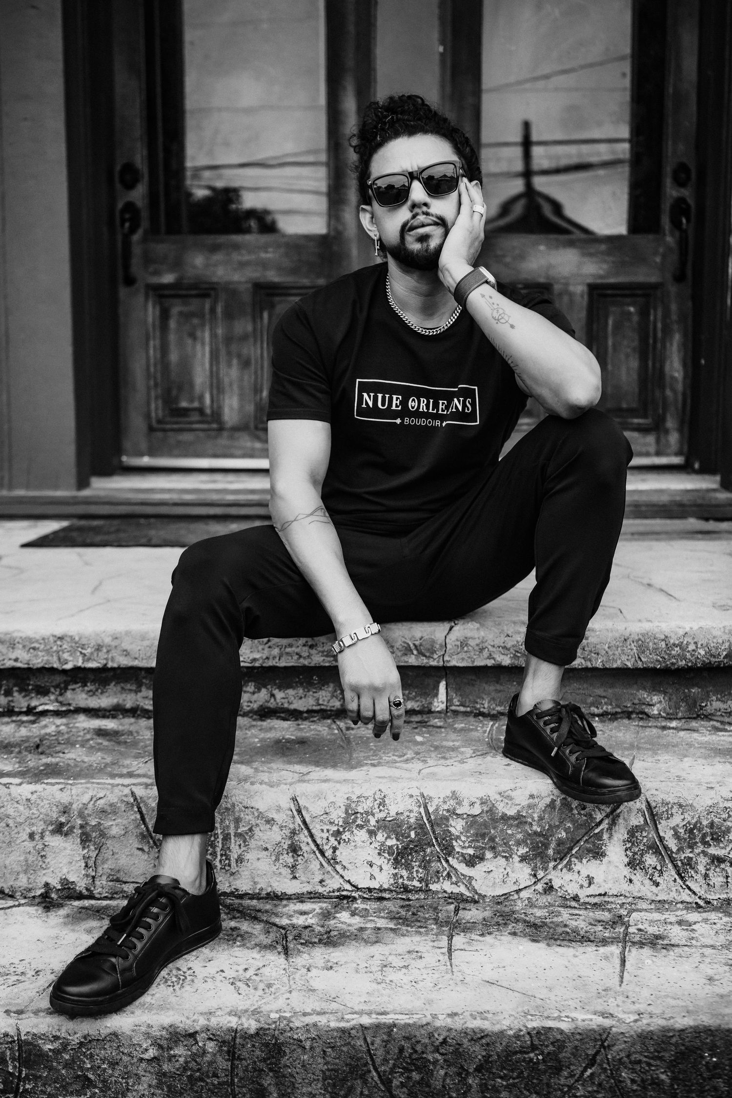 Street fashion portrait of someone in black attire sitting on concrete steps.