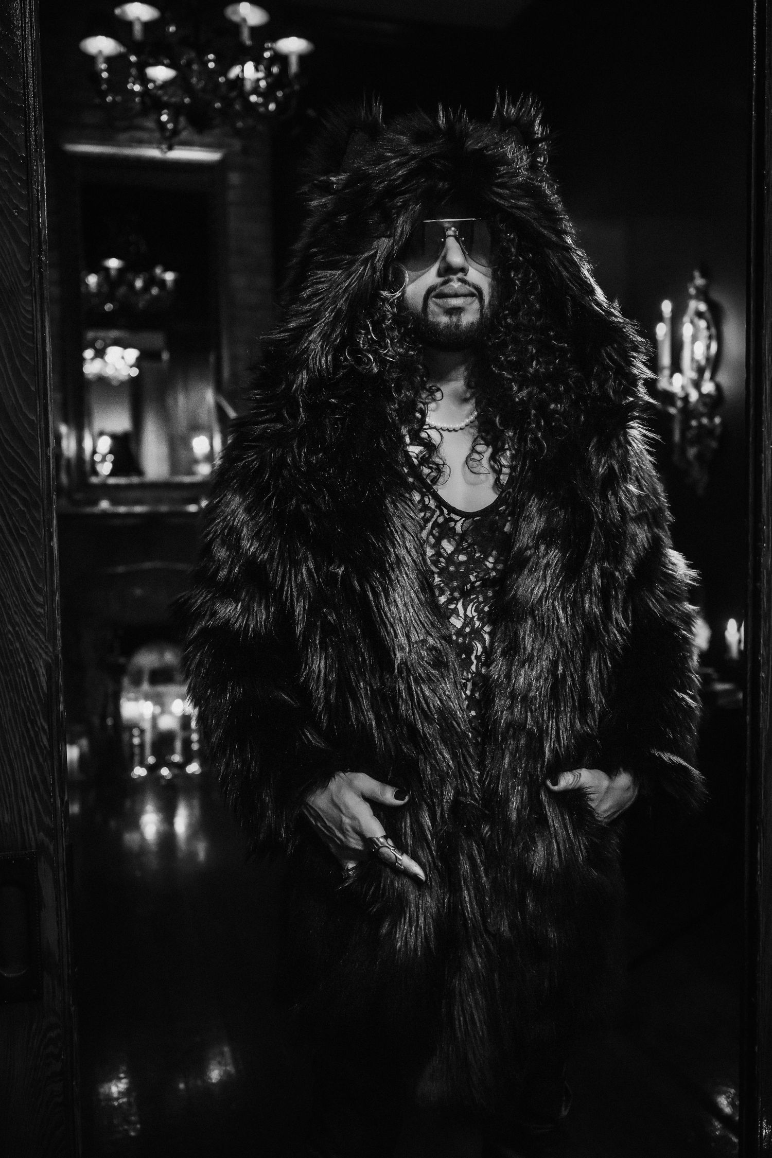Portrait of someone in a luxurious fur coat standing in a dimly lit elegant interior.