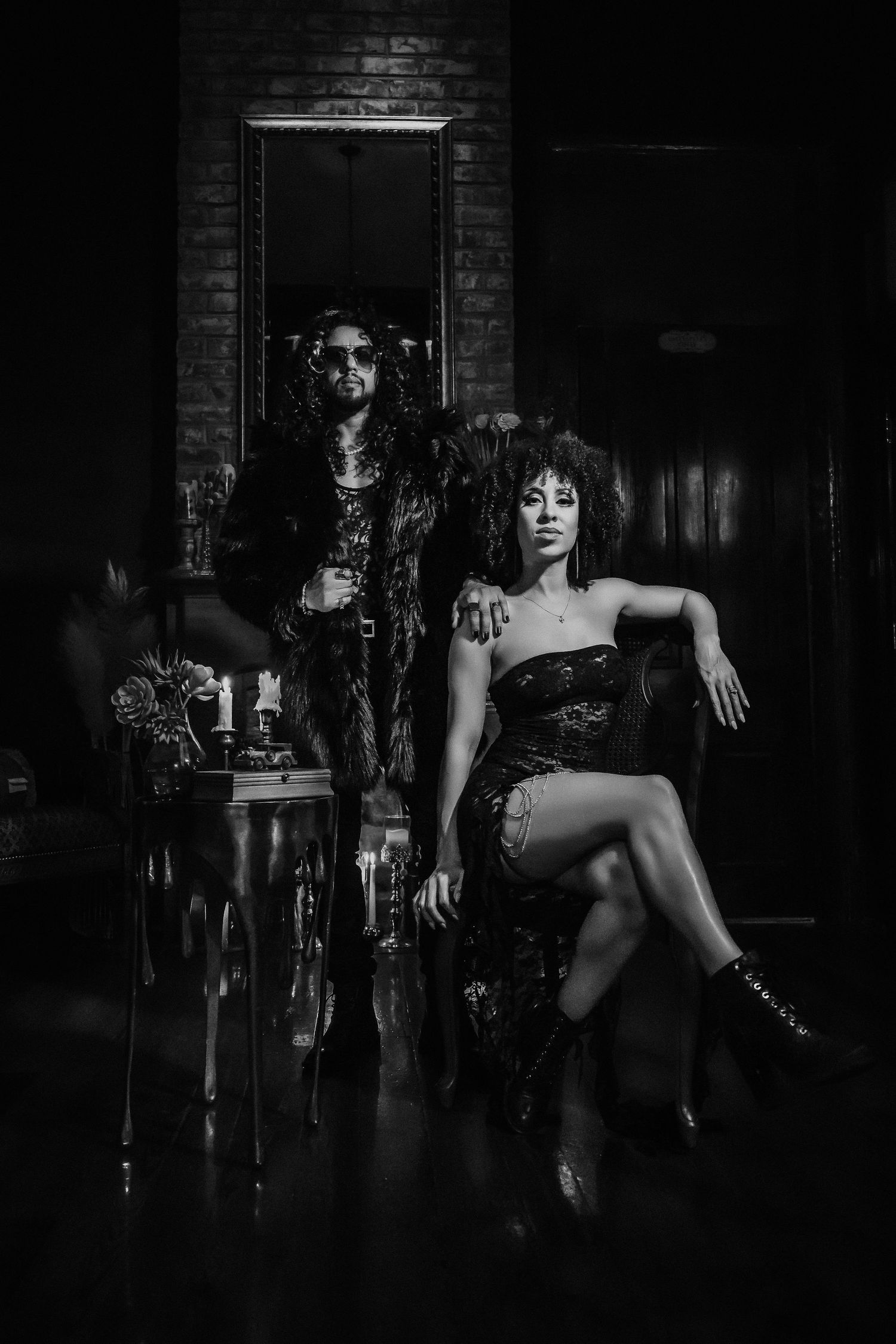 Dramatic black and white boudoir photo of two models posing in a dark vintage-style setting.