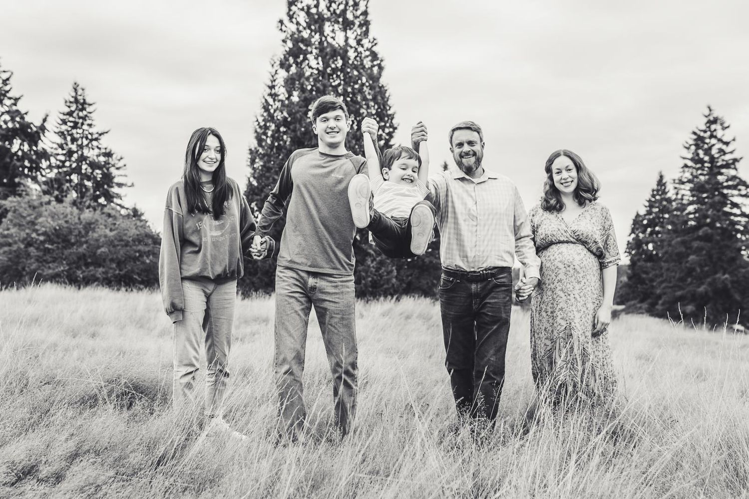 Black and white photo of a family swinging their child in a grassy field