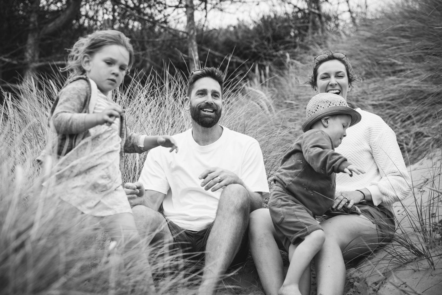 A black and white portrait of a family relaxing in beach grass.