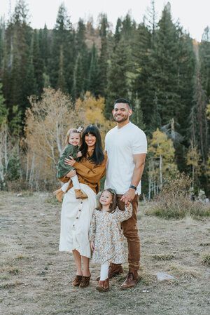 Outdoor family portrait session in autumn forest setting with coordinated earth-tone outfits.