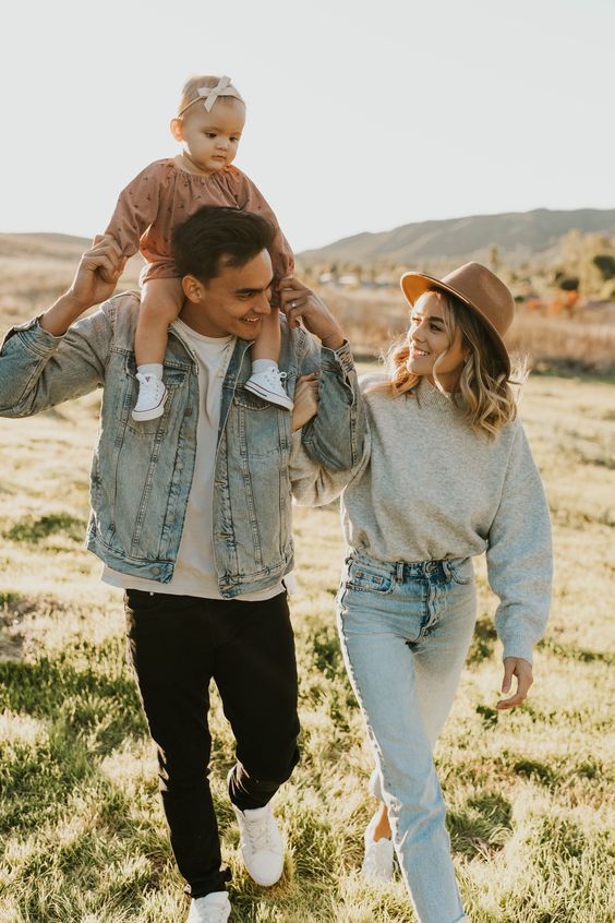 Casual family outfit coordination in denim and neutral tones walking through a grassy field at sunset.