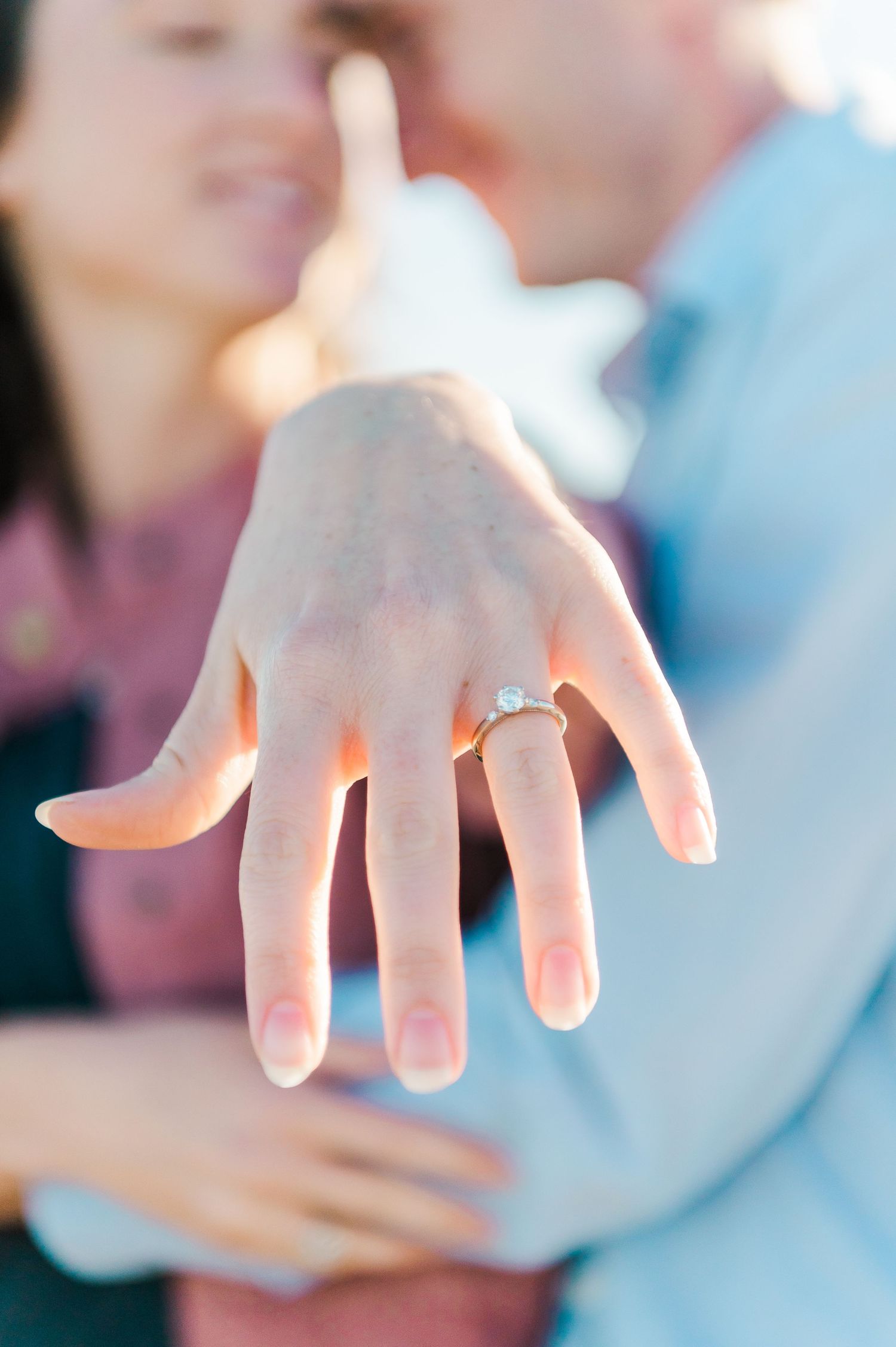 A close-up shot of a hand displaying an engagement ring against a soft-focus background.