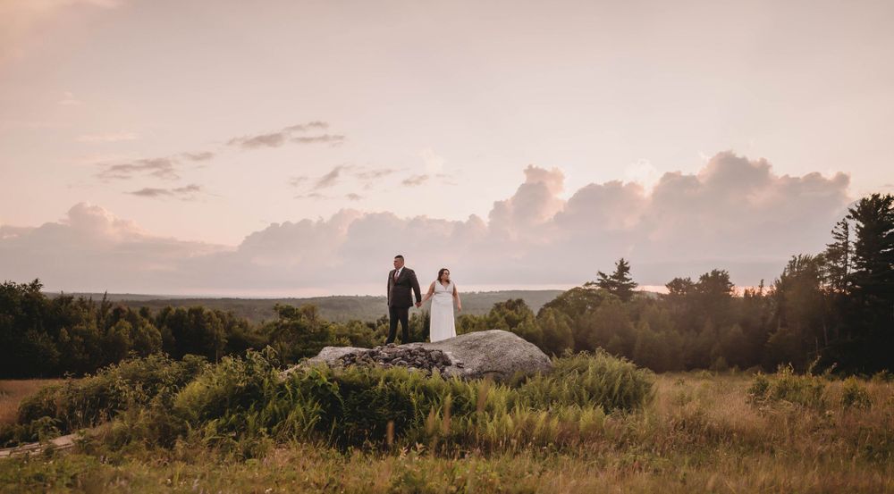 A couple stands on a hilltop against a sunset sky during their wedding photoshoot.