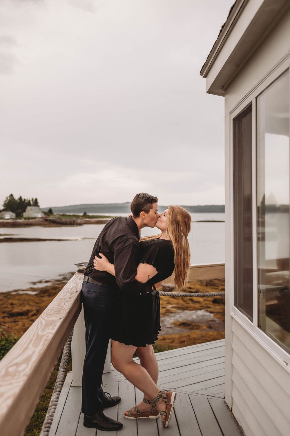 Romantic couple embracing on coastal deck with ocean view during sunset.