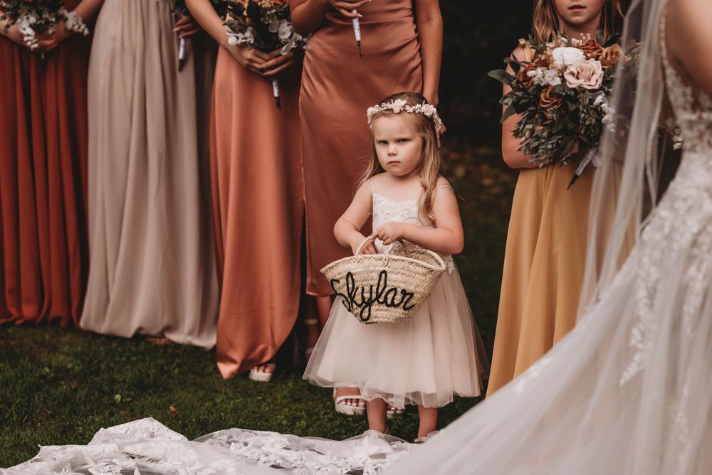 Flower girl in pink dress holds decorative basket during wedding ceremony.
