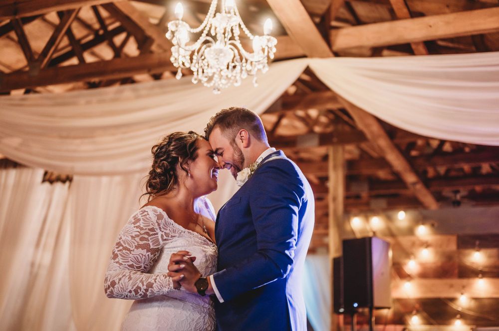 A romantic first dance moment under a decorated rustic barn ceiling with chandelier and draped fabric.