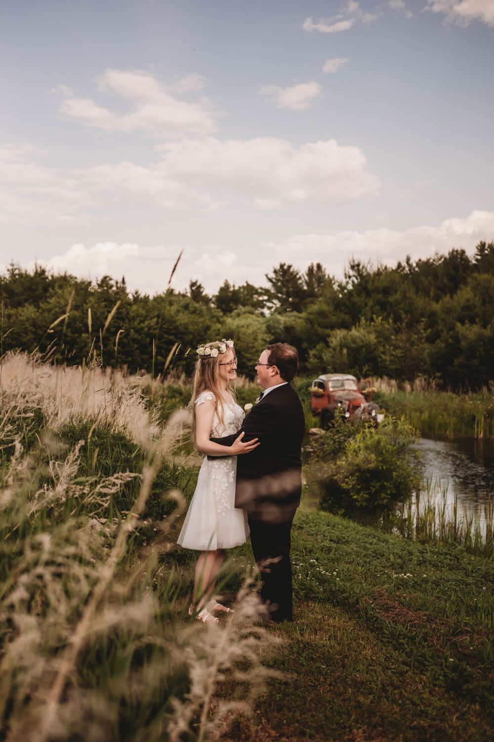 A tender moment between a couple surrounded by tall grass and pine trees near a lake.