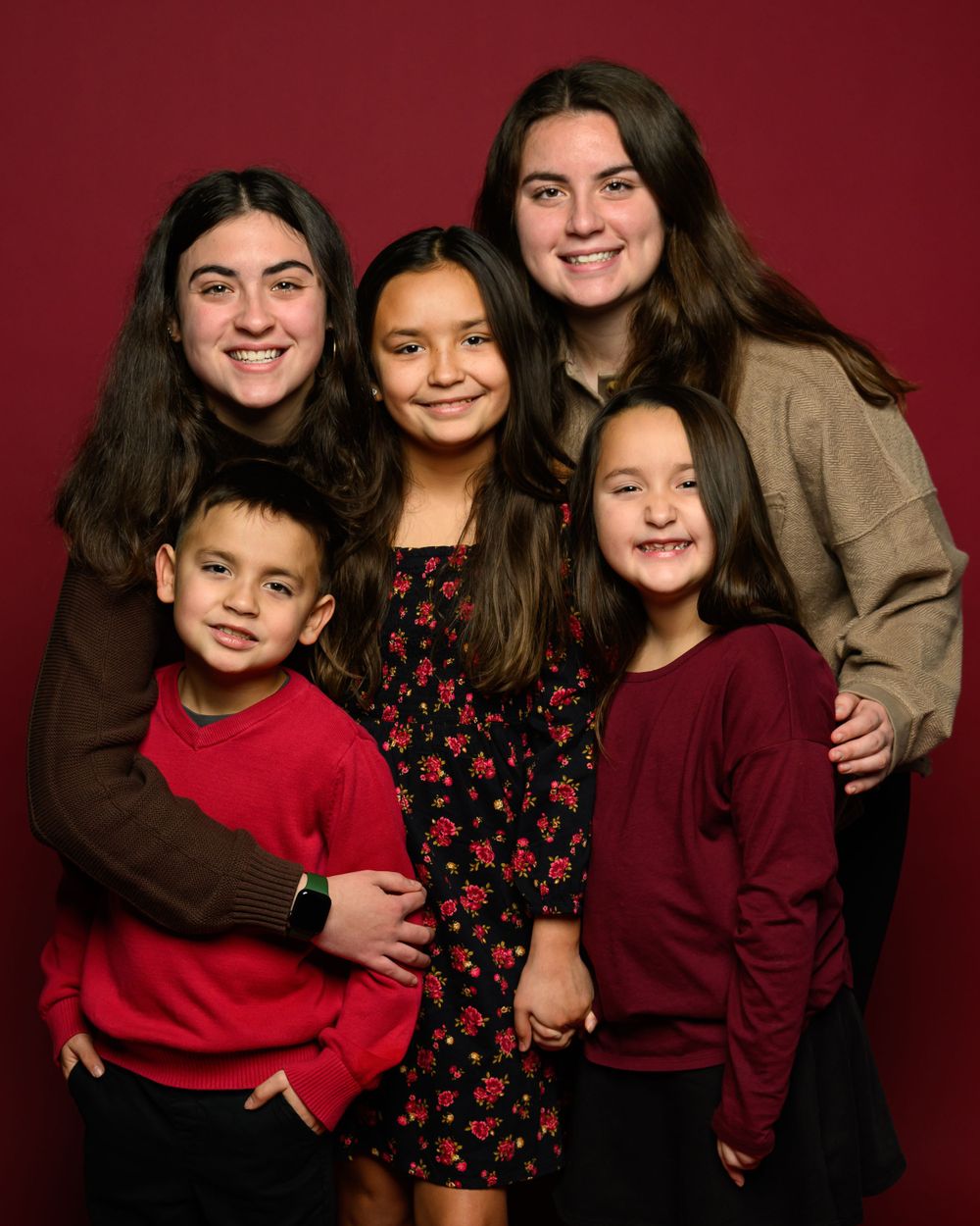 Family portrait series against burgundy background wearing coordinated red and black outfits.