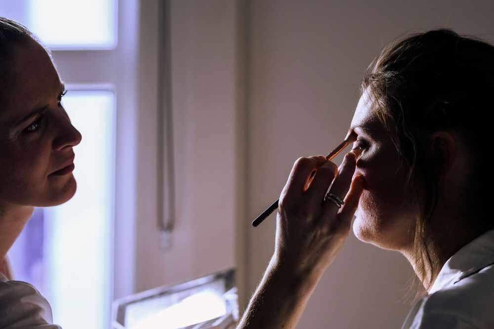 Makeup artist applying cosmetics in soft window light.