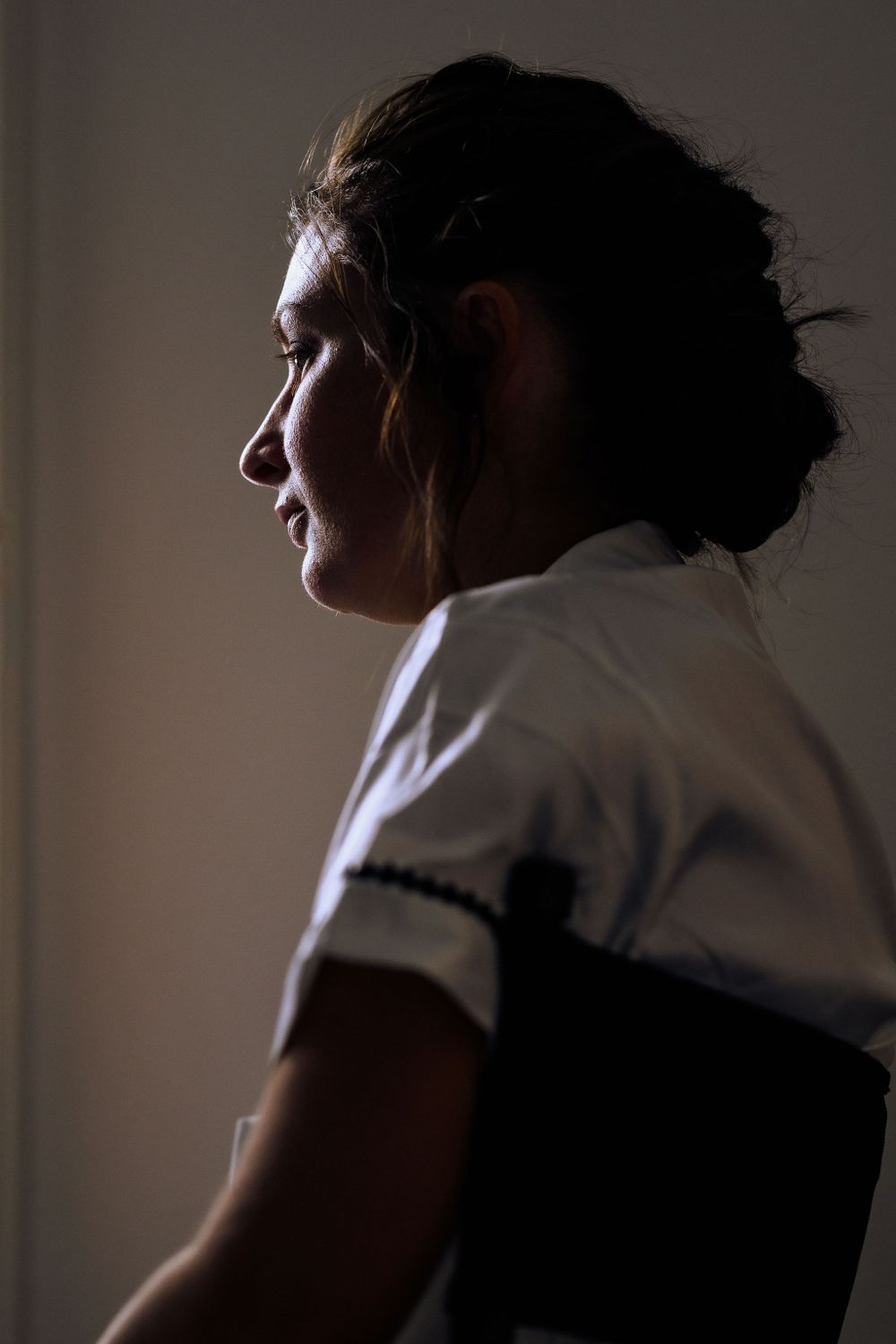 Side profile of person in white shirt against minimalist background.