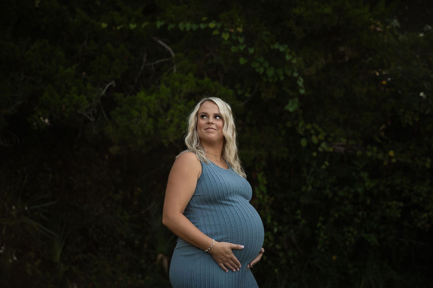Maternity photos showing pregnant belly in blue dress against natural outdoor backdrop.