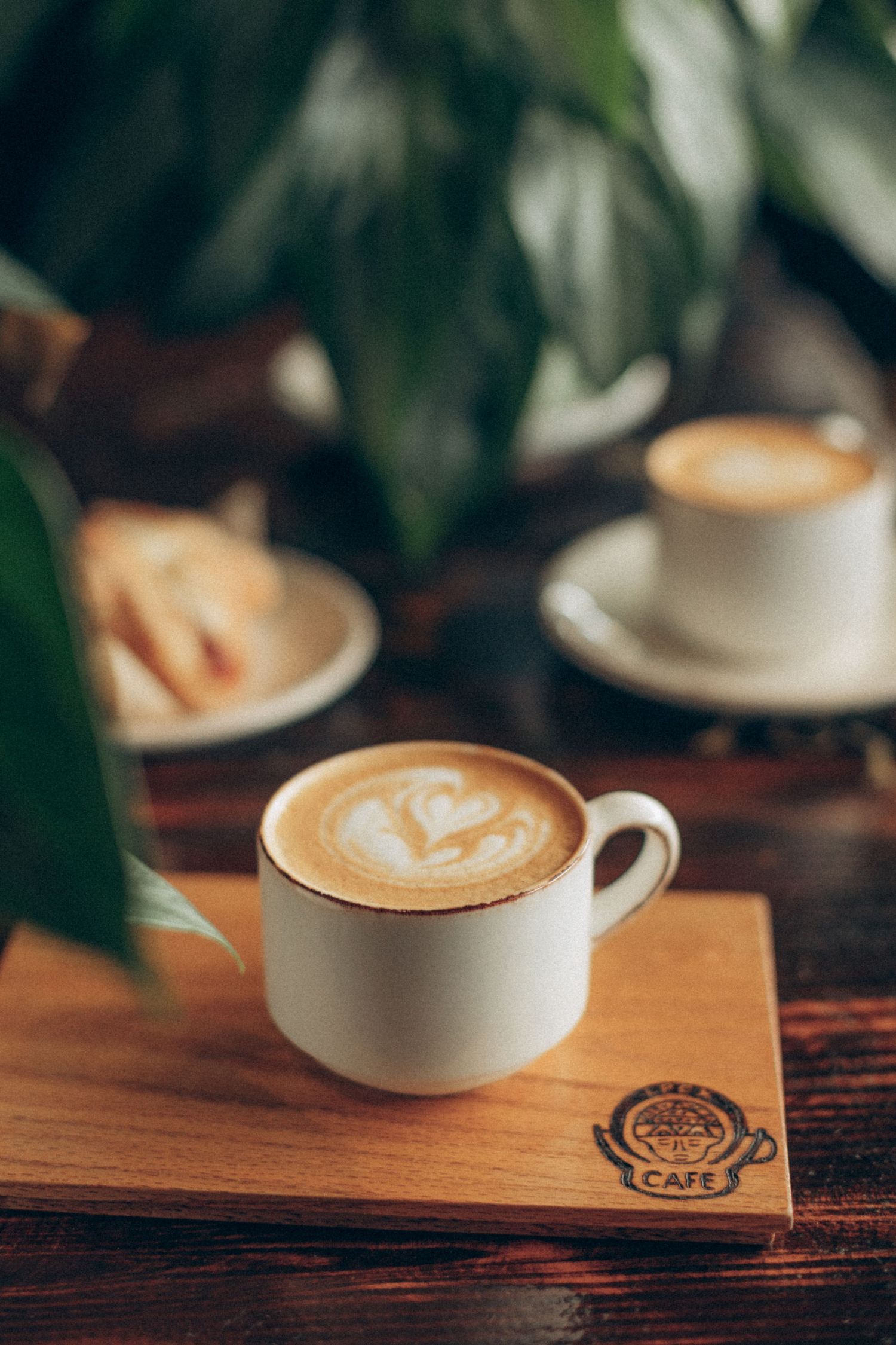 White coffee cup with latte art heart design on wooden table with cafe logo.