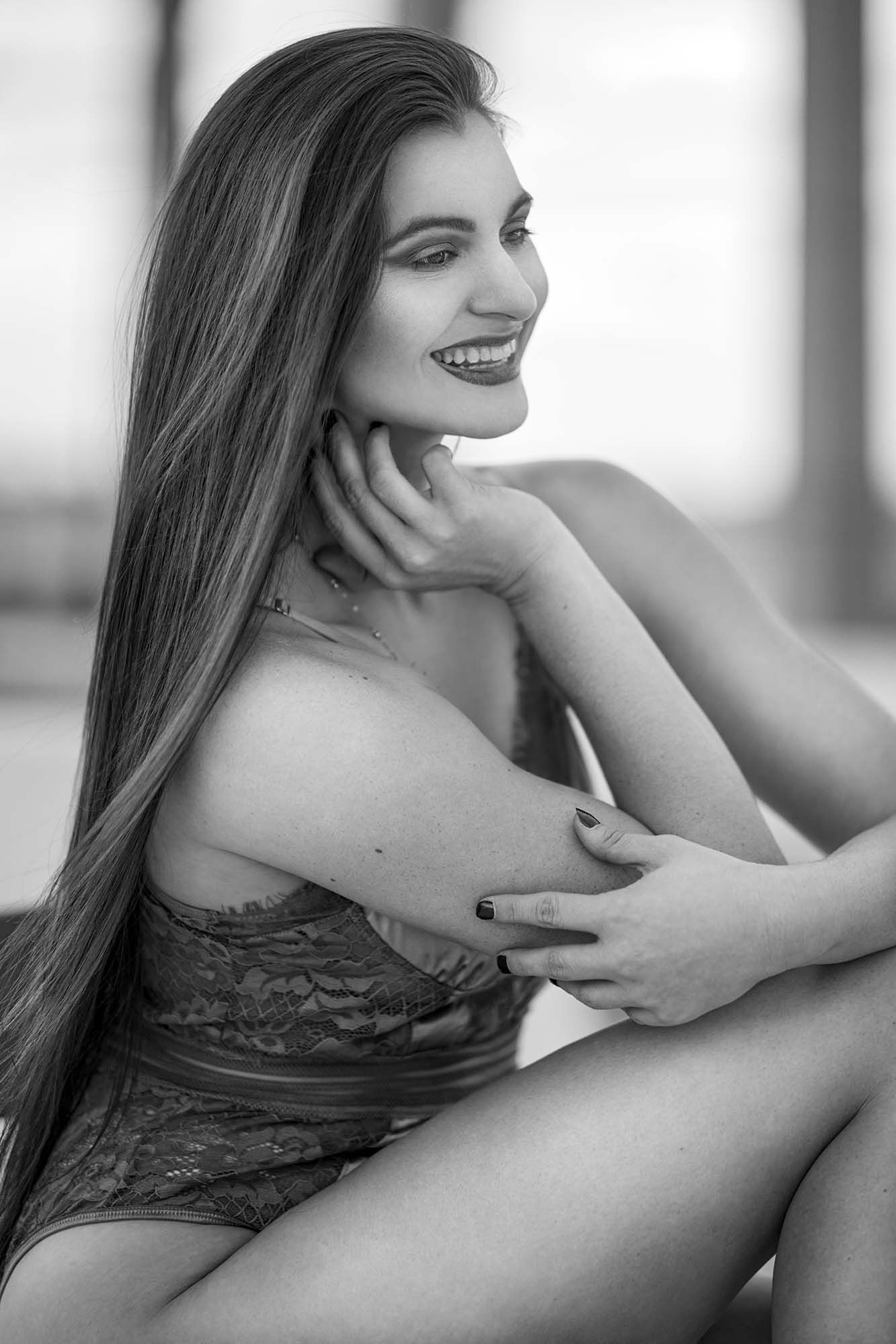 Black and white boudoir portrait of a model in lace posing by a window.