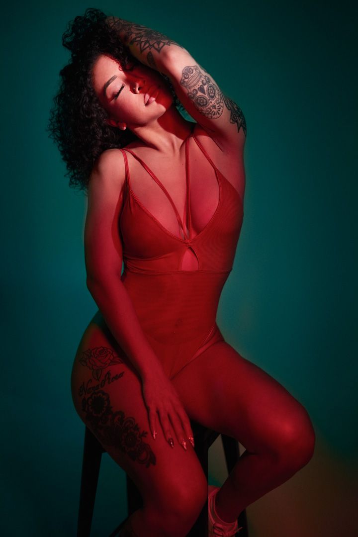 Dramatic boudoir photography with red lighting and tattoo details against a dark background.