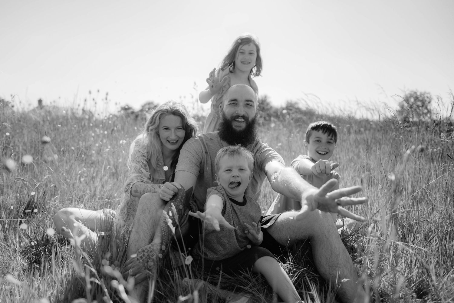 A group sits together in a field of tall grass on a sunny day, captured in black and white.