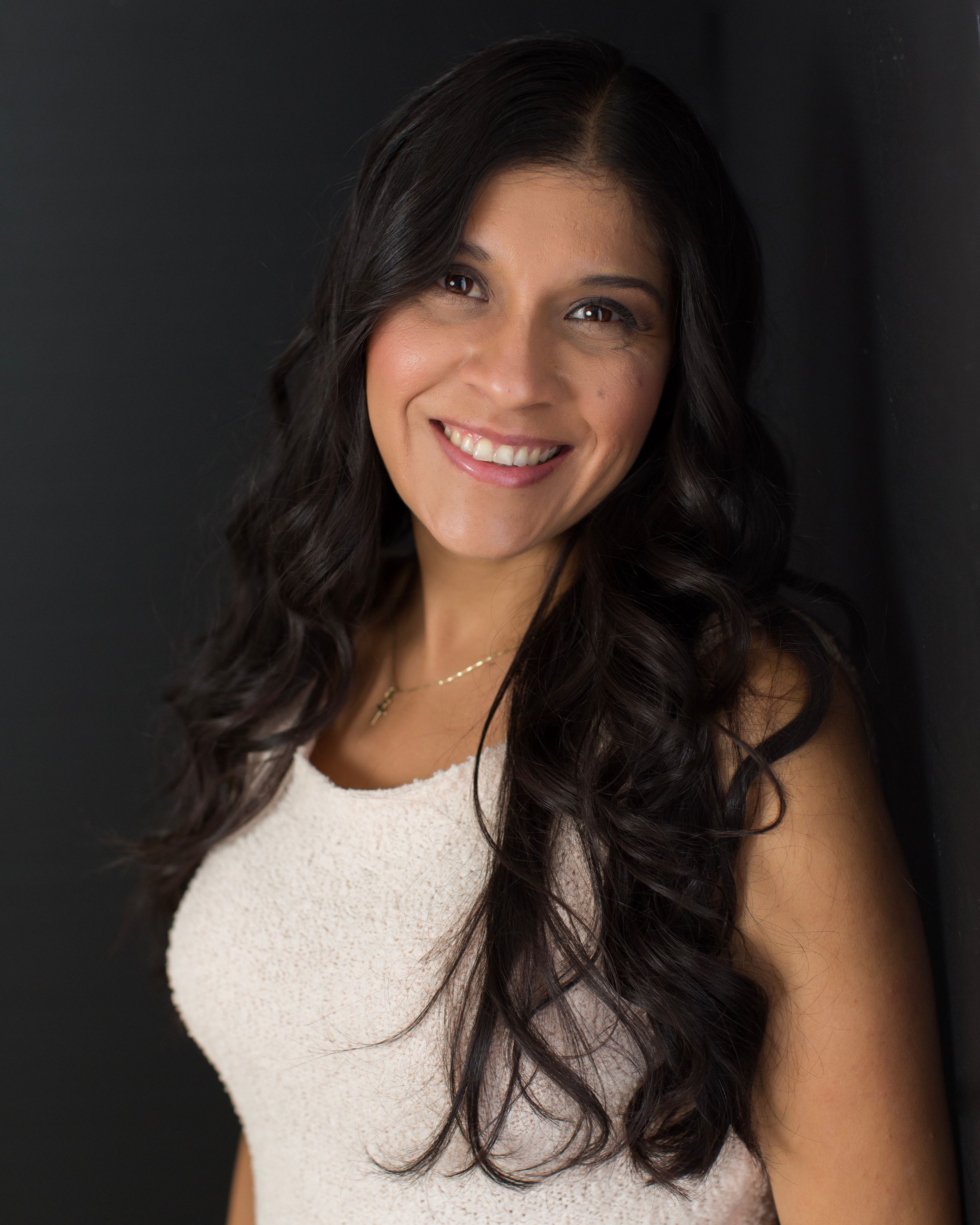 Professional studio portrait with person in white top and long dark wavy hair.