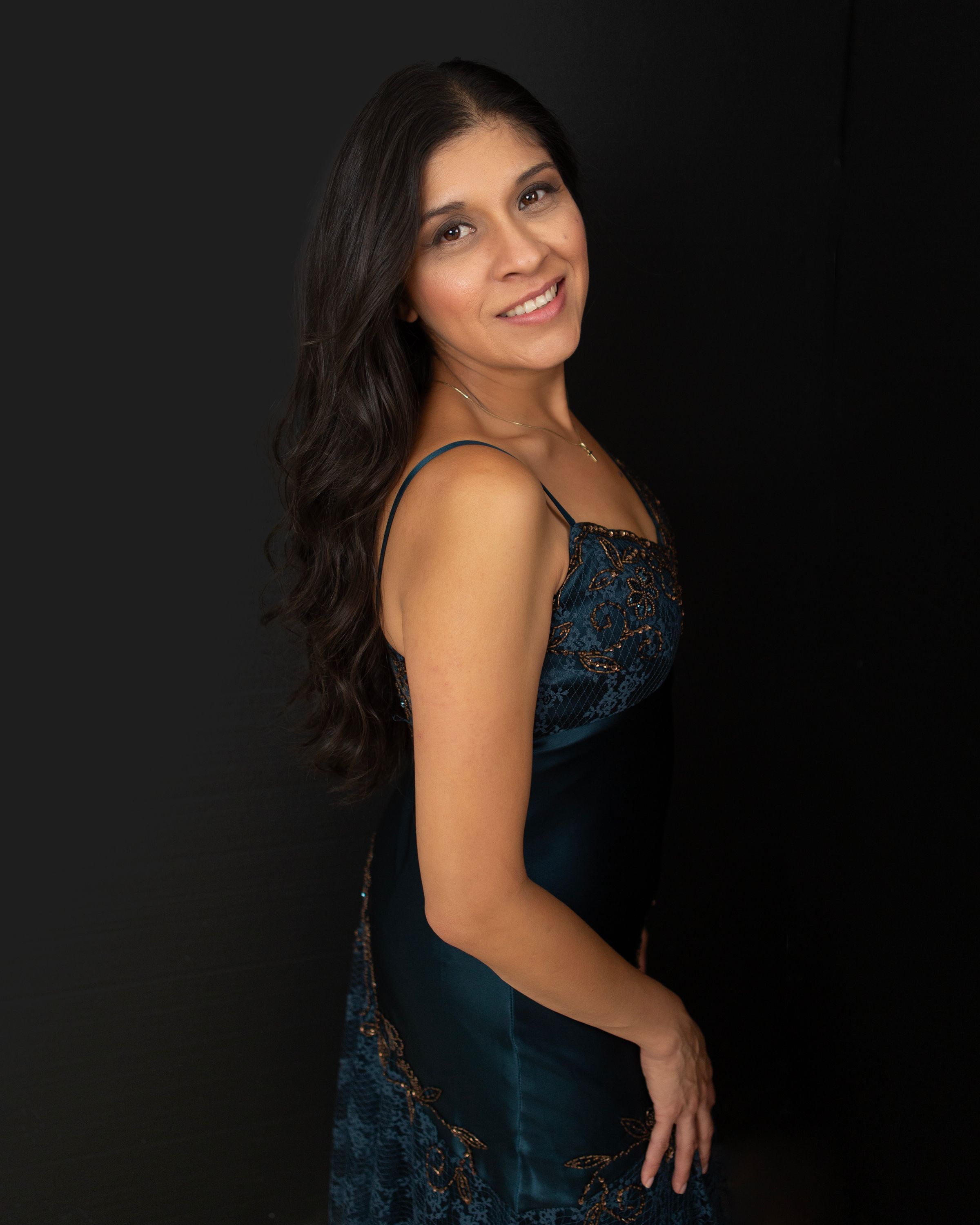 Studio portrait of person in dark blue lace dress posed against black background.