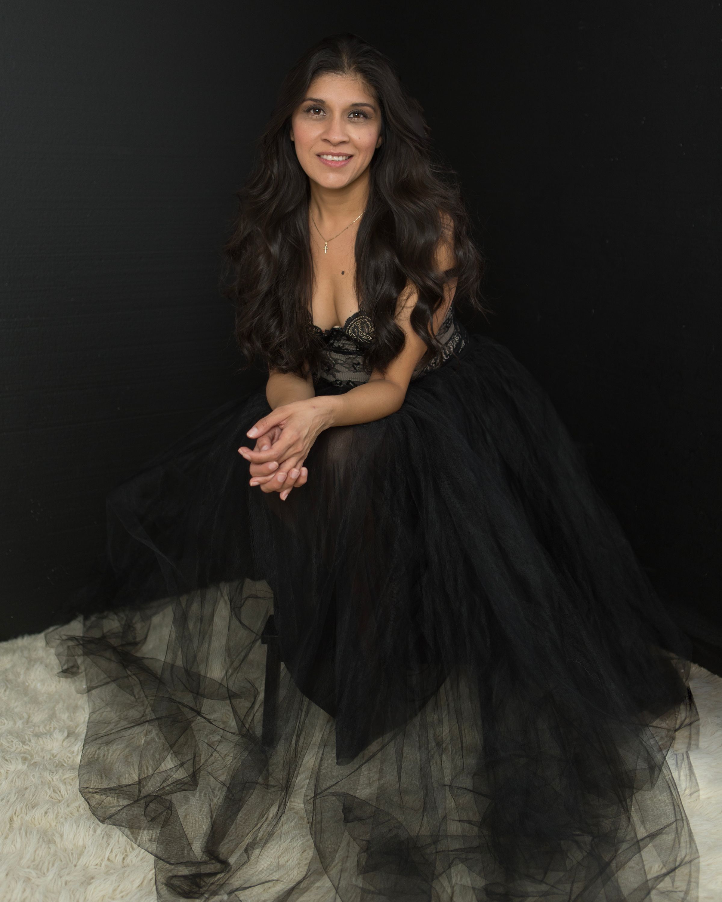 Woman in black tulle dress posing playfully on dark background.