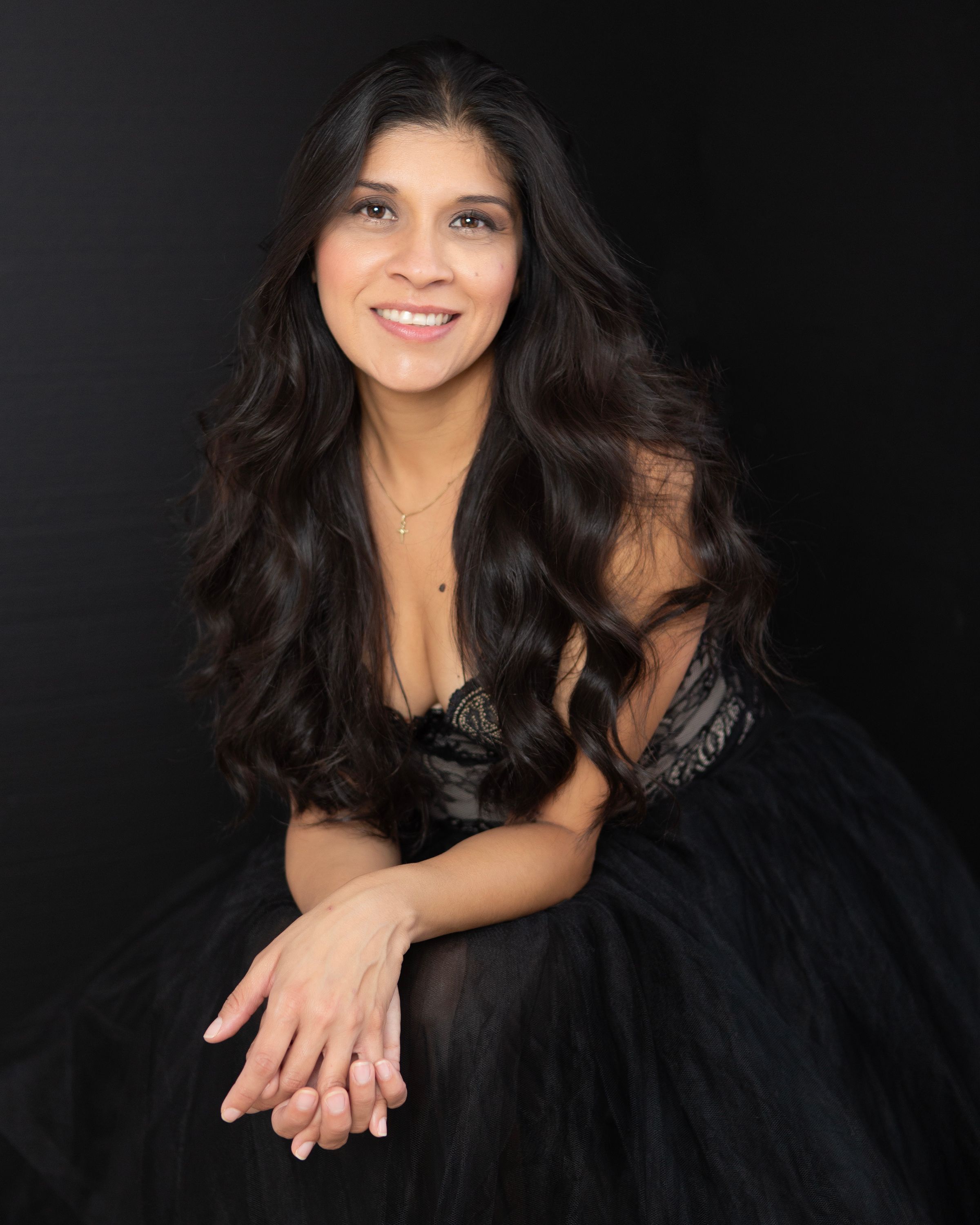 Woman with long dark hair in black dress against dark backdrop.