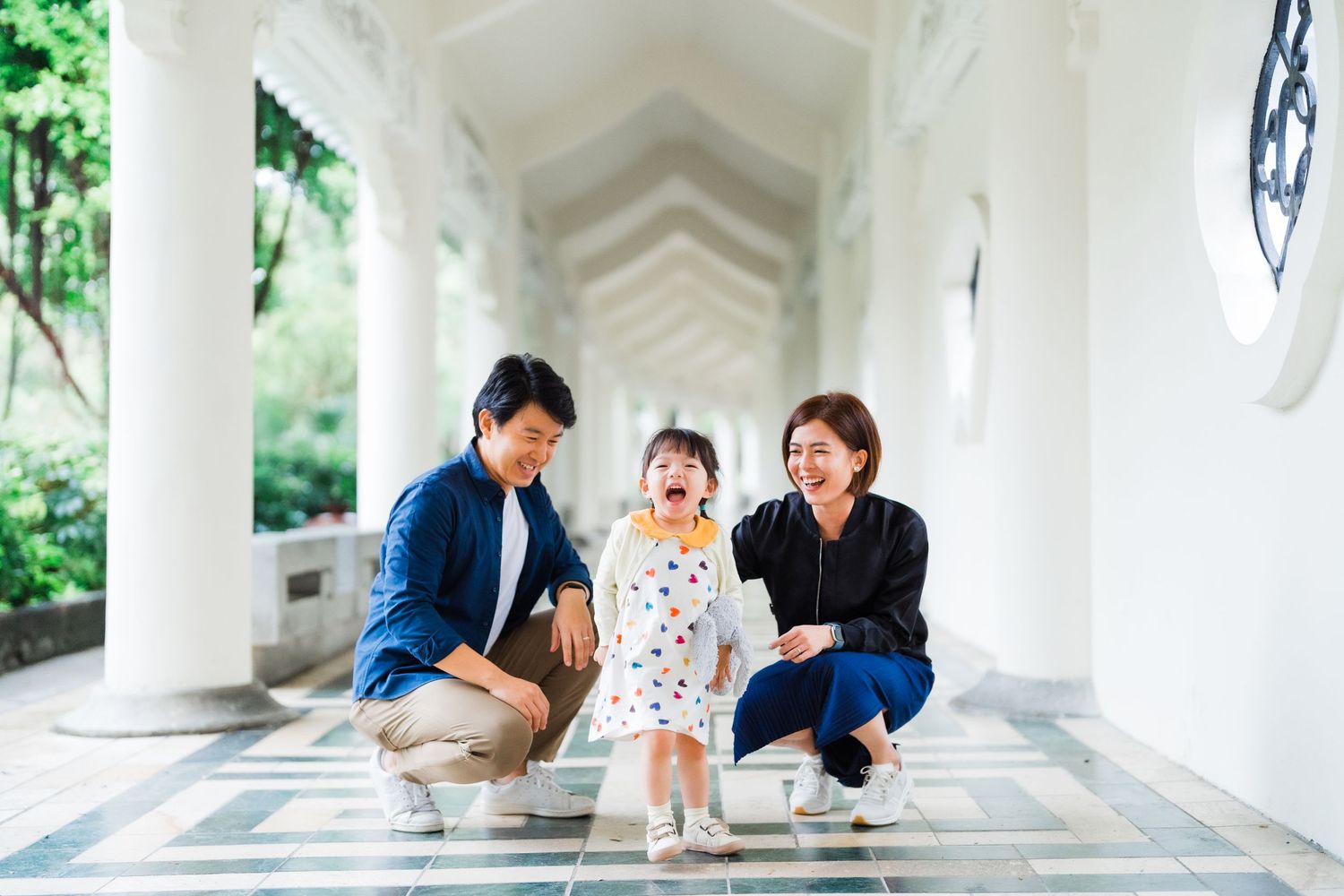A family kneeling together on a white columned corridor with ornate floor tiles.